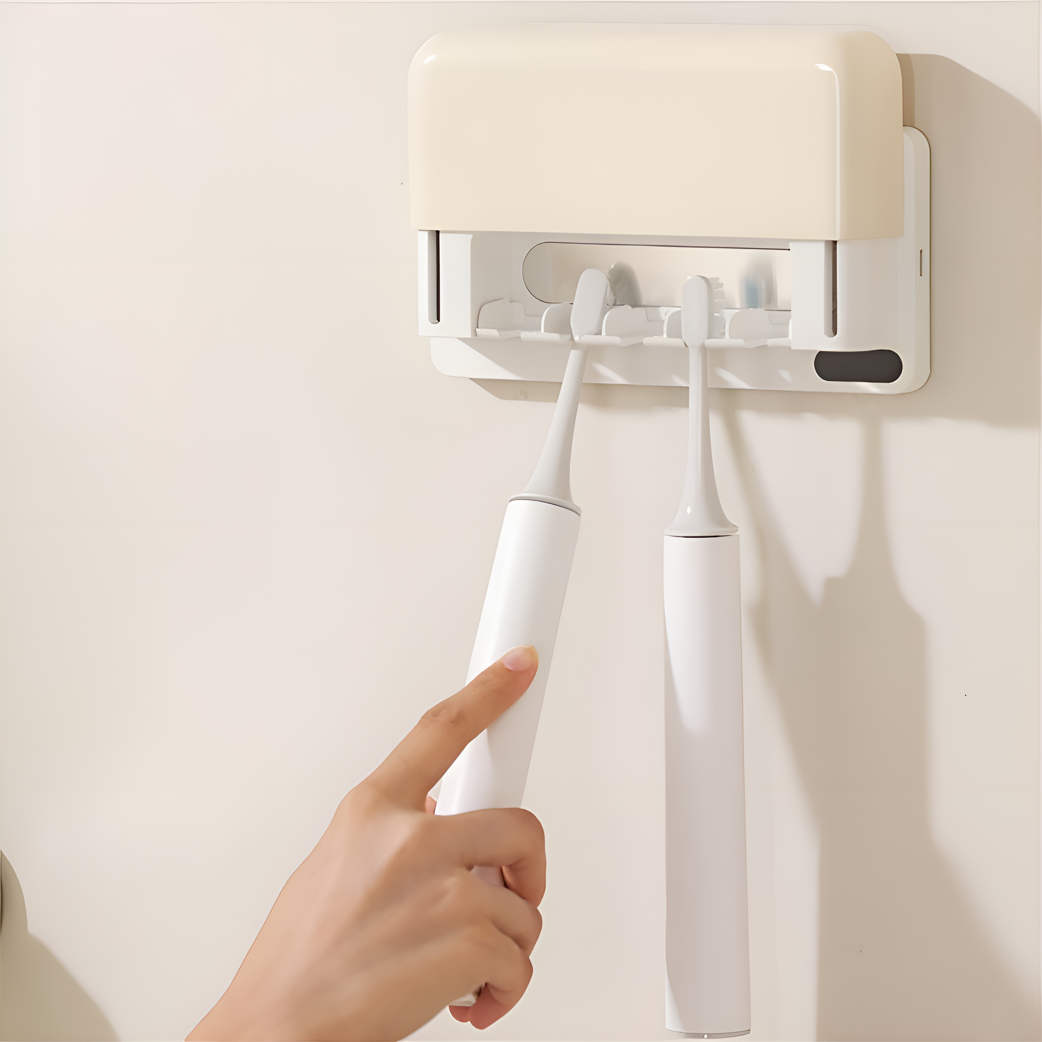 Zwei weiße elektrische Zahnbürsten in einem beigefarbenen Wandhalter, Hand.
