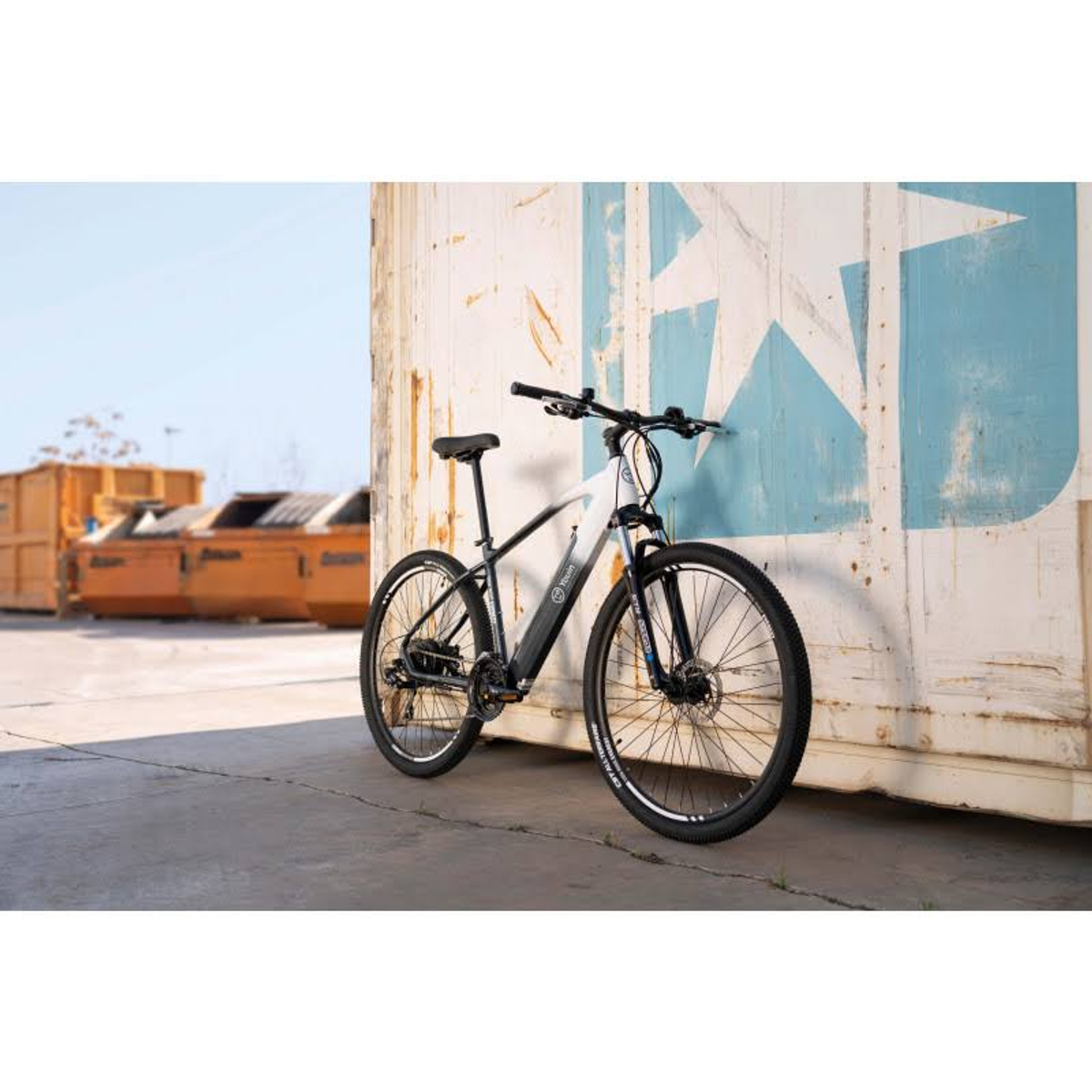 Czarno-biały rower górski oparty o biały kontener. Błękitne niebo i tło przemysłowe.