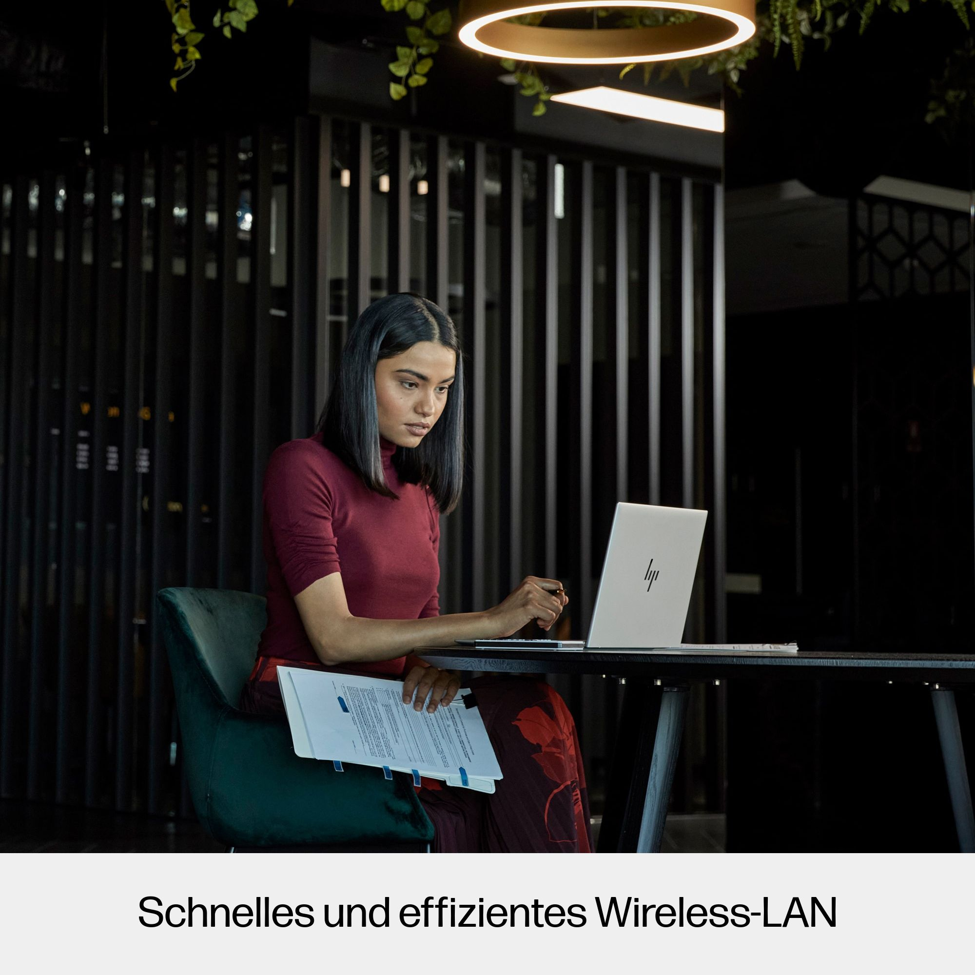 Kobieta pracująca na laptopie, z dokumentami i ciemnym tłem, w nowoczesnym otoczeniu biurowym.