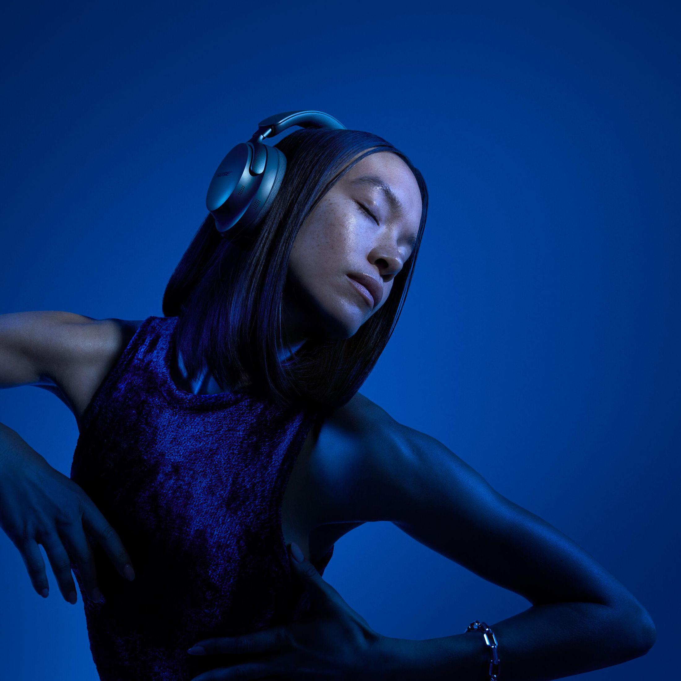 Kobieta ze słuchawkami, zamknięte oczy, w niebieskim świetle. Ma fioletowy top.