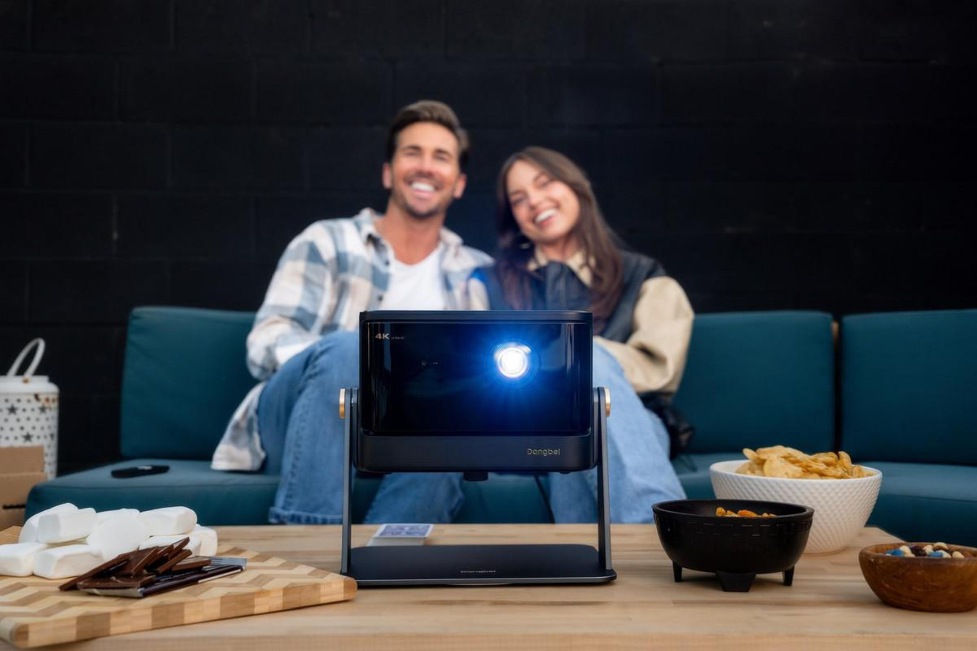 Mężczyzna i kobieta siedzą na kanapie, patrząc na ekran projektora.