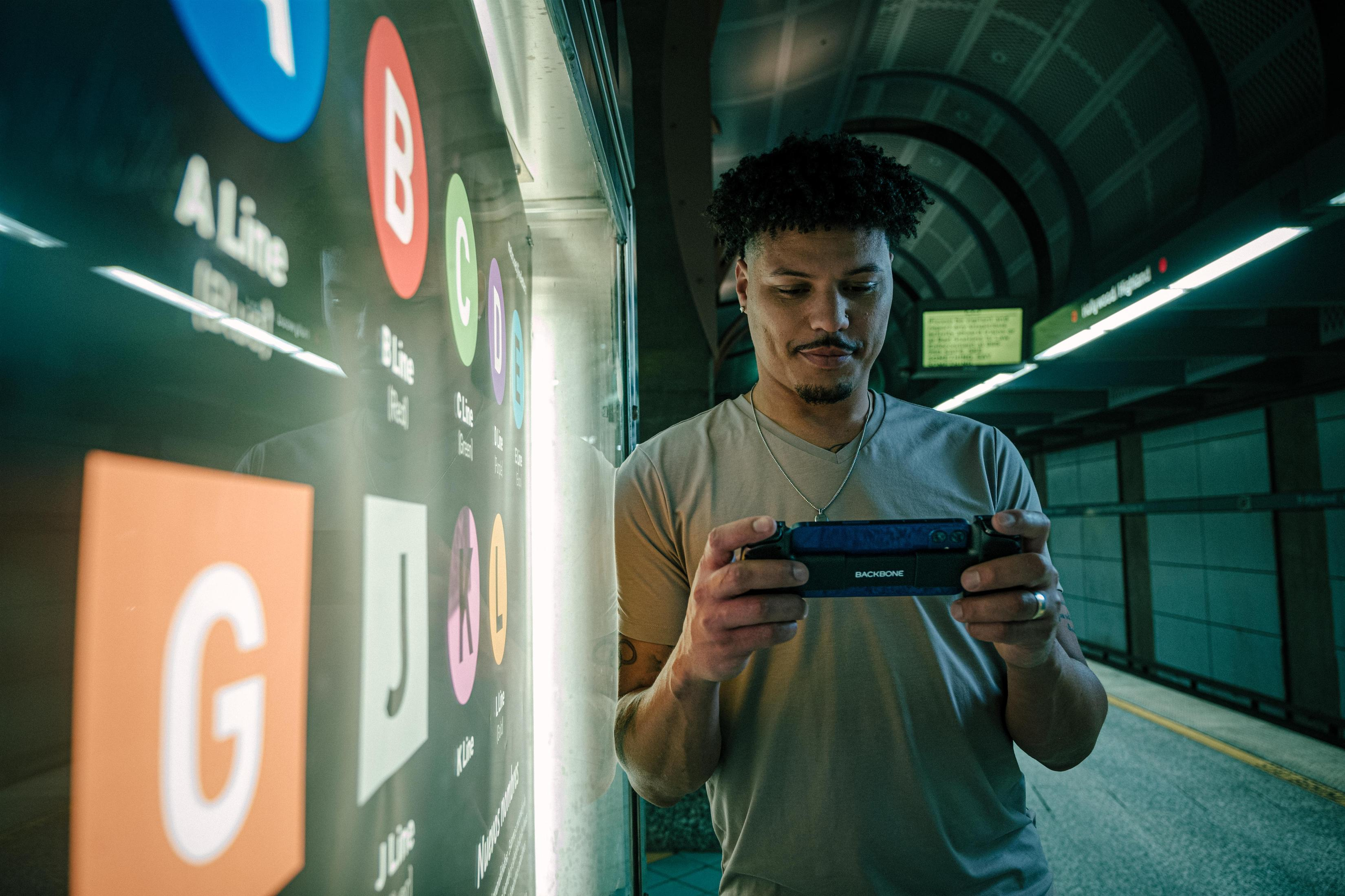Ein Mann hält ein Spielgerät in einer U-Bahn-Station und blickt auf den Bildschirm.