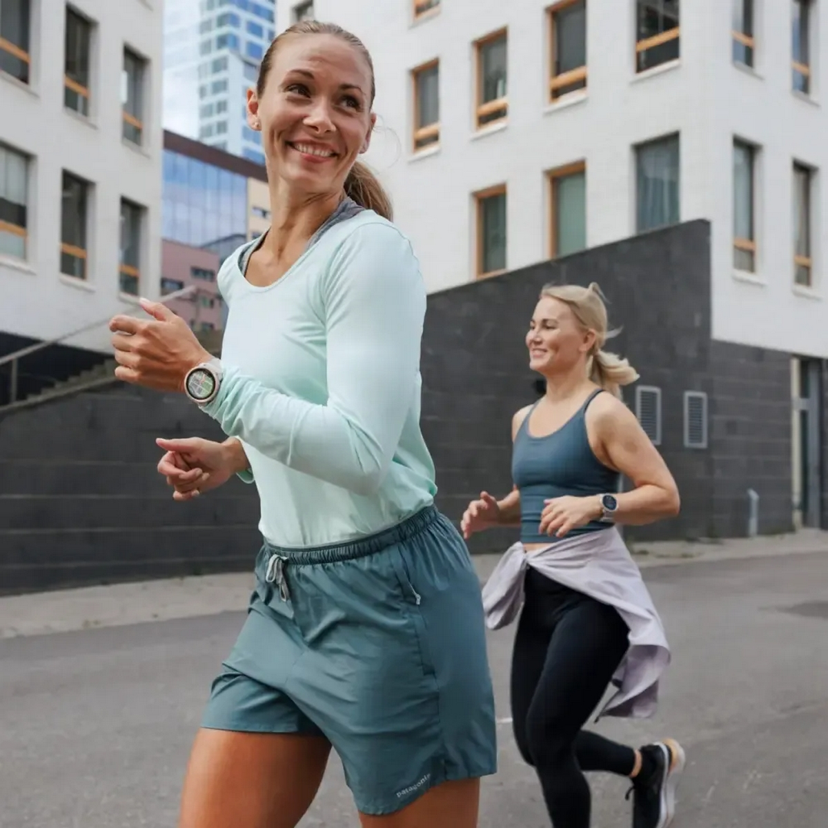 Dwie kobiety biegnące razem ulicą. Jedna patrzy wstecz, uśmiechając się.