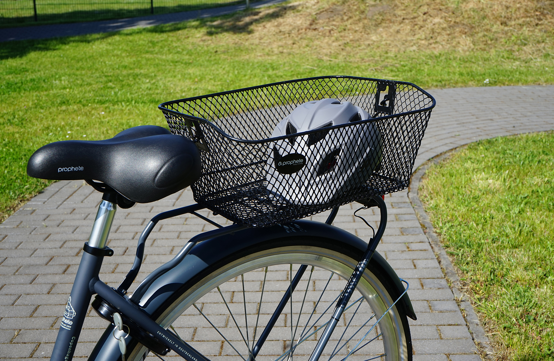 Ein Fahrrad mit einem Korb mit einem Helm. Das Fahrrad steht auf einem Ziegelsteinweg.