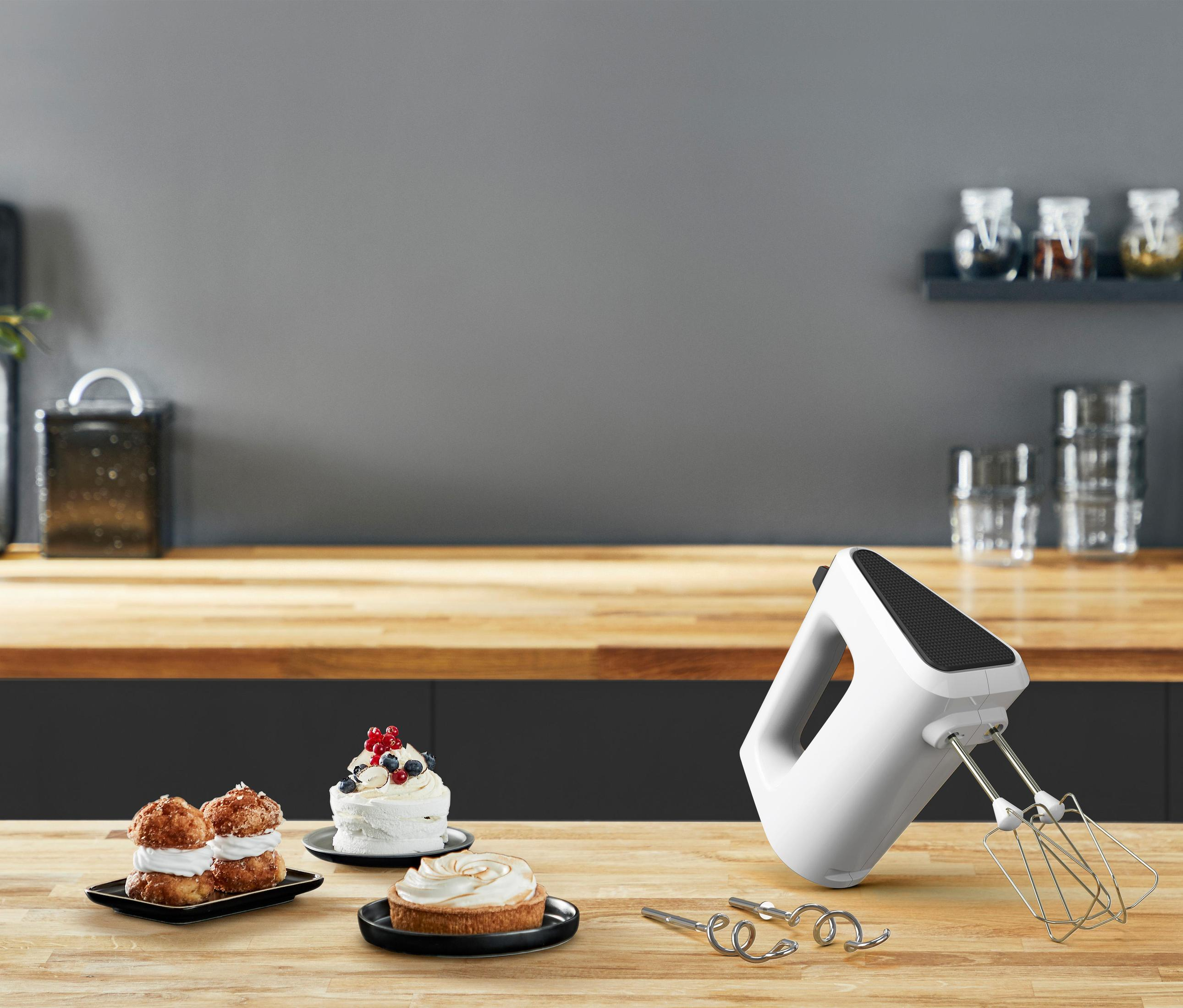 Witte handmixer met cake en gebak op een houten aanrecht. Grijze achtergrond.