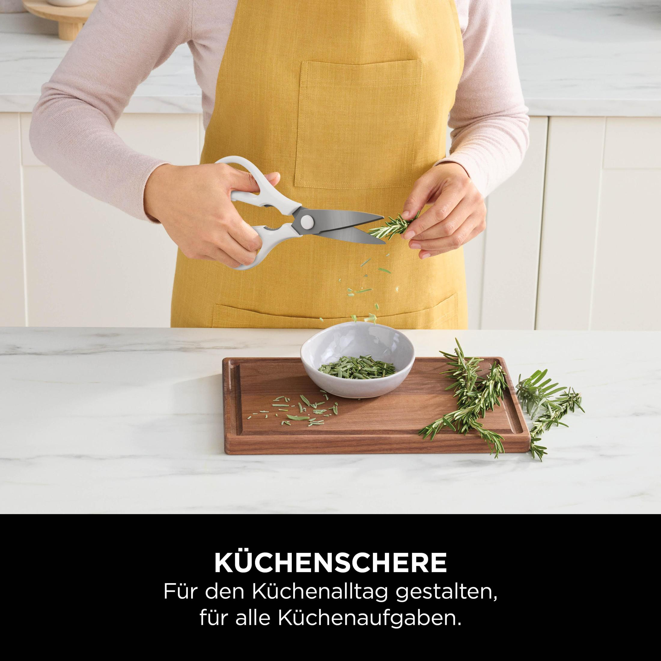 Eine Person schneidet Rosmarin mit einer Küchenschere auf einem Holzbrett. Eine Schüssel und Rosmarinzweige sind vorhanden.