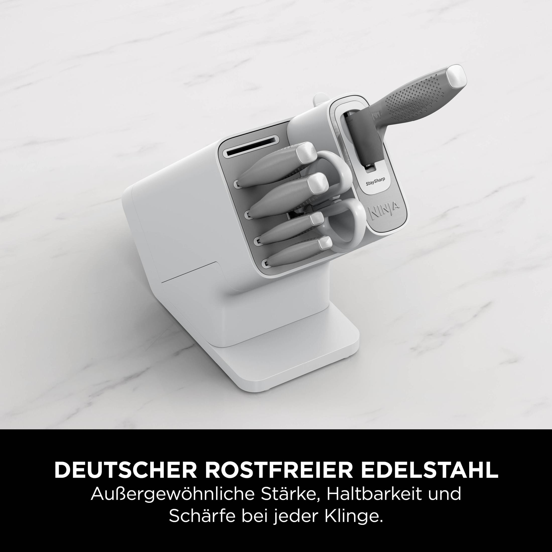 Ein weißer Messerblock mit grauen Messern. Der Block hat ein Ninja-Logo. Auf einer marmorähnlichen Oberfläche.