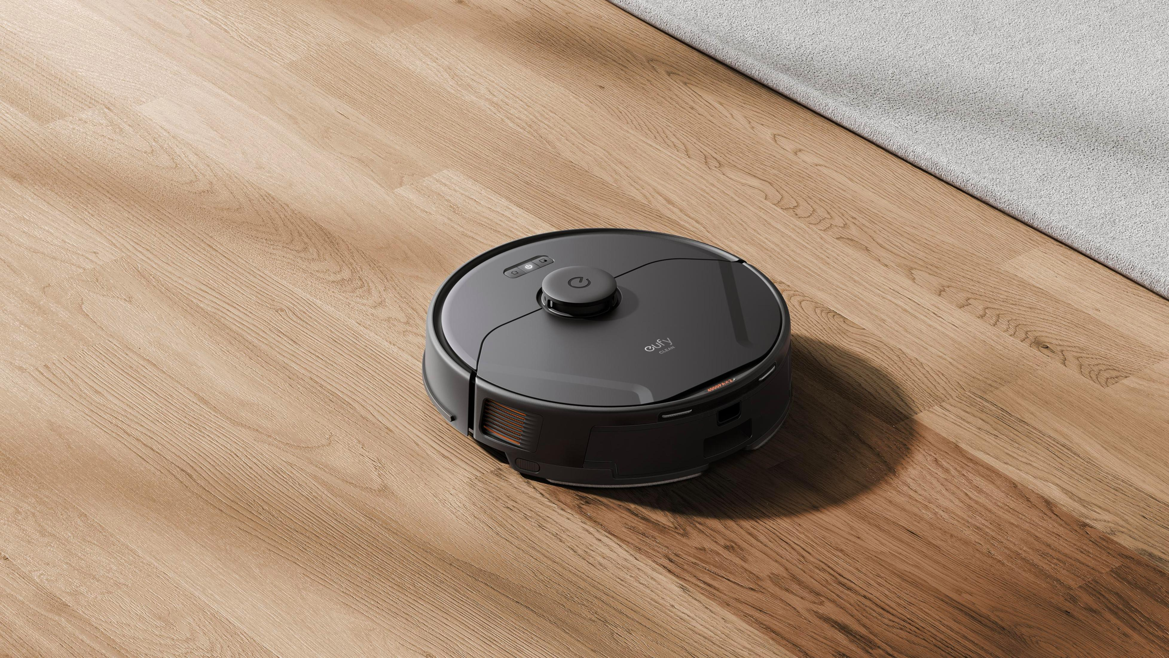 Roboter-Staubsauger auf einem Holzboden mit einem Teppich. Der Staubsauger ist schwarz und rund.