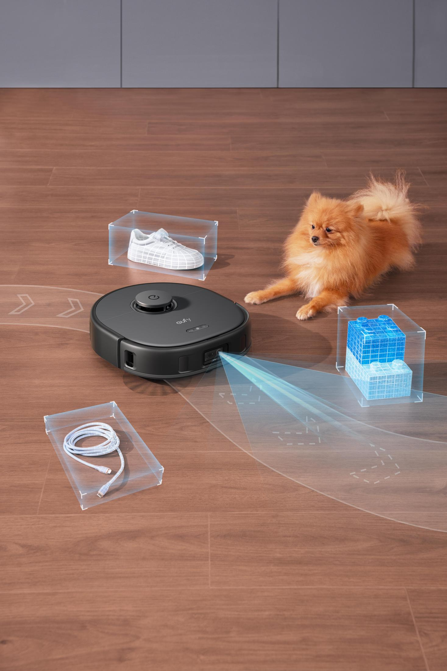 Robot sprzątający na drewnianej podłodze, z psem i przedmiotami w pudełkach.