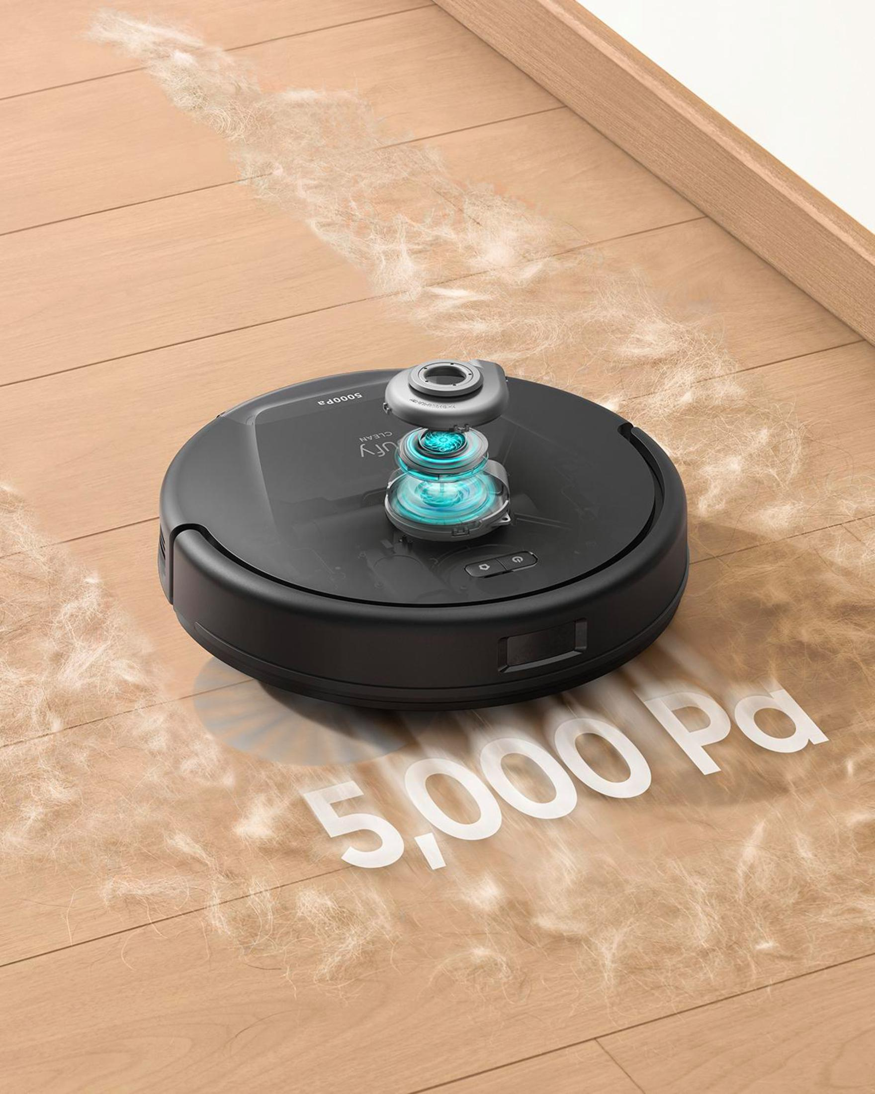 Czarny robot sprzątający na drewnianej podłodze, z widocznym kurzem i tekstem '5,000 Pa'.
