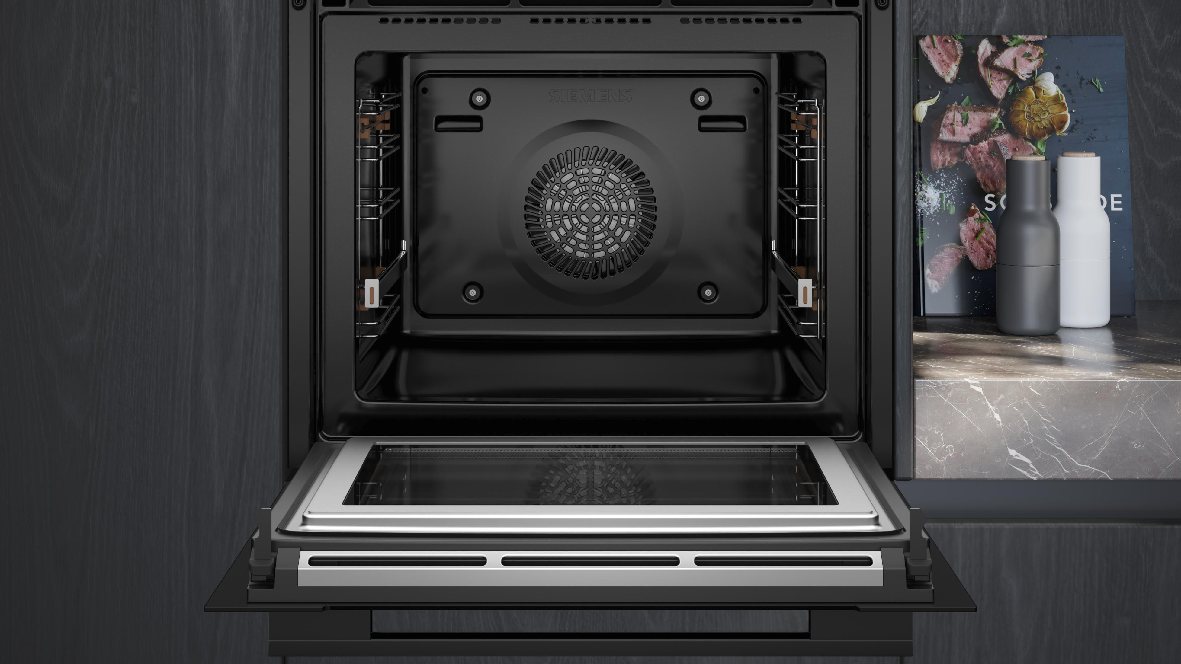 Open oven met een ventilator binnenin. Zwart interieur. Ovendeur staat open. Donkere achtergrond.