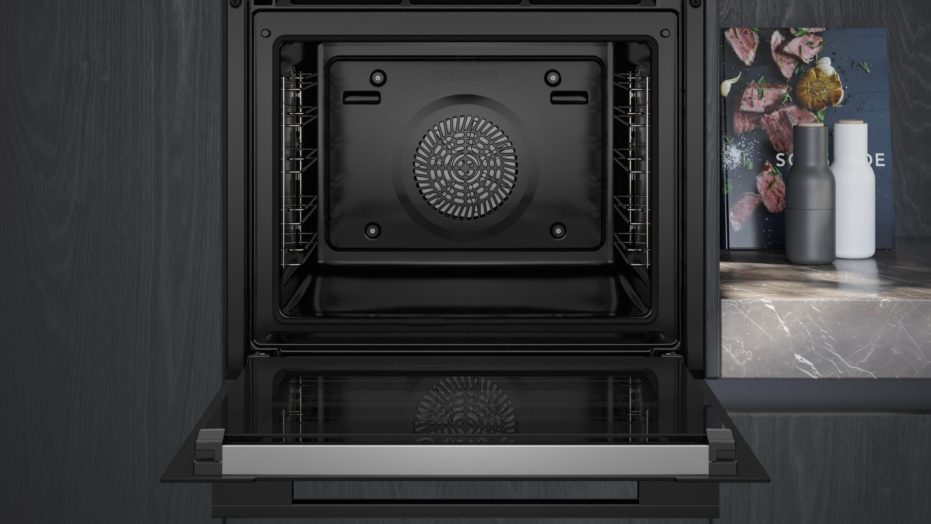 Een open oven die de binnenkant laat zien, met een glazen deur. Een kookboek en zout- en pepervaatjes zijn in de buurt.