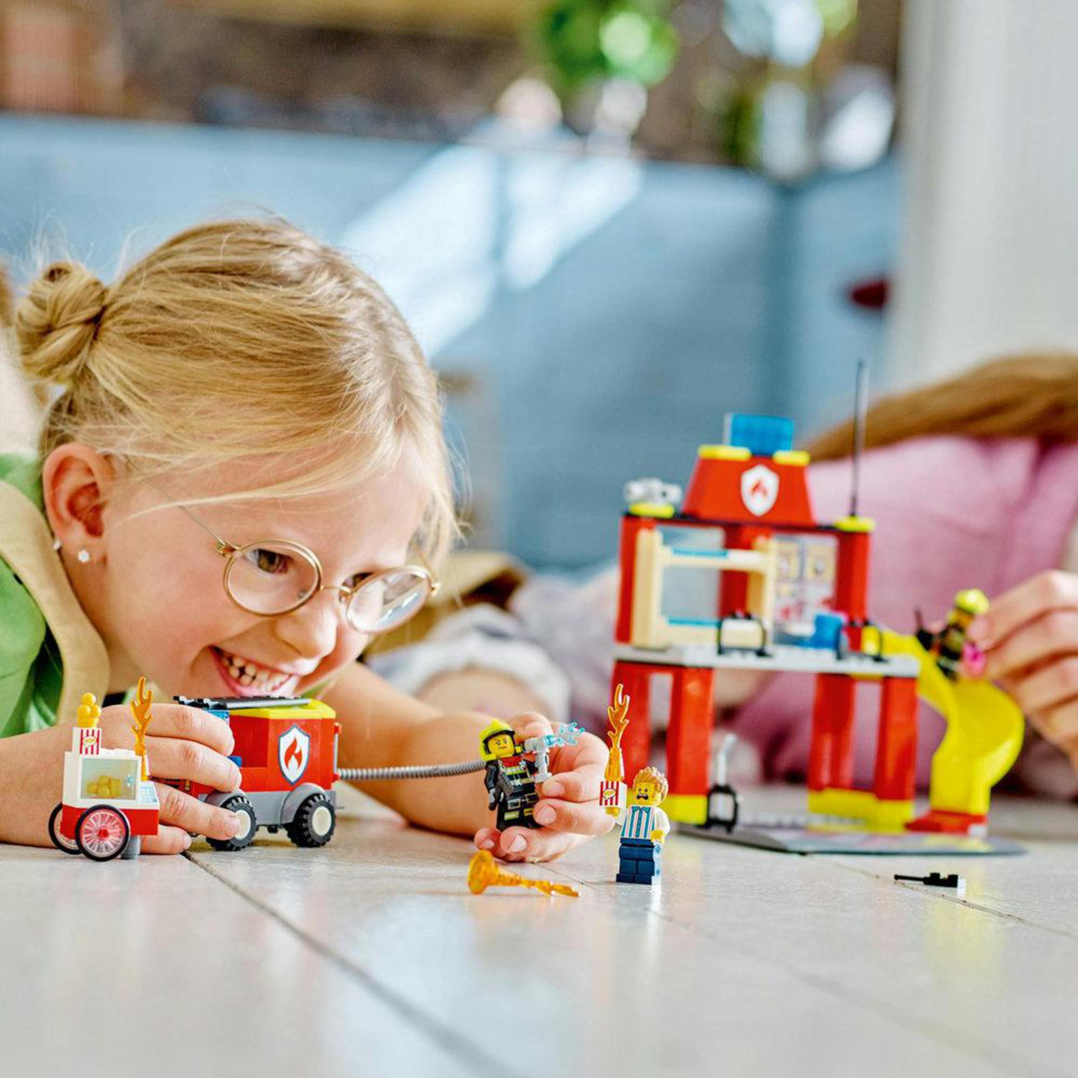 Una niña juega con un set LEGO de rescate de bomberos. El set incluye un camión de bomberos, una estación y figuras.