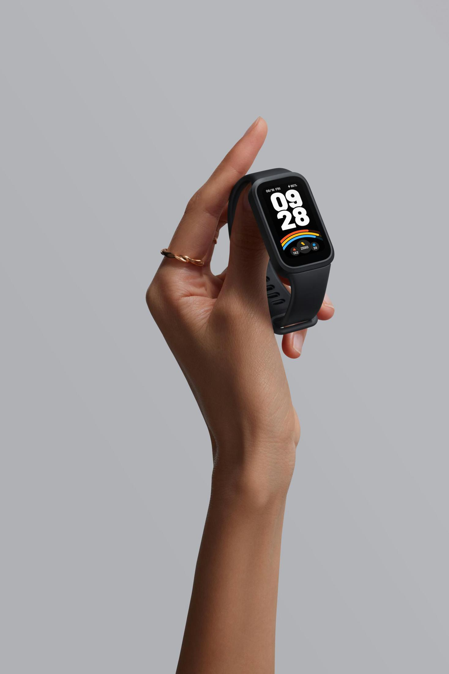Die Hand einer Person, die eine schwarze Smartwatch hält, auf der das Datum und ein Regenbogensymbol angezeigt werden.