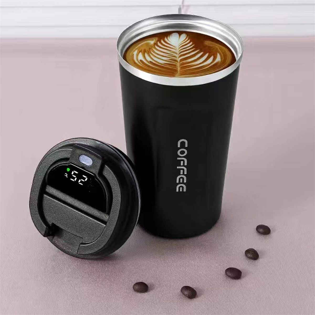 Ein schwarzer Kaffeebecher, Deckel und Kaffeebohnen auf pinker Oberfläche mit Latte Art.