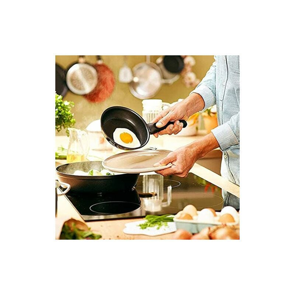 Person hält eine Pfanne mit Spiegelei. Küchenhintergrund mit anderen Pfannen und Essen.