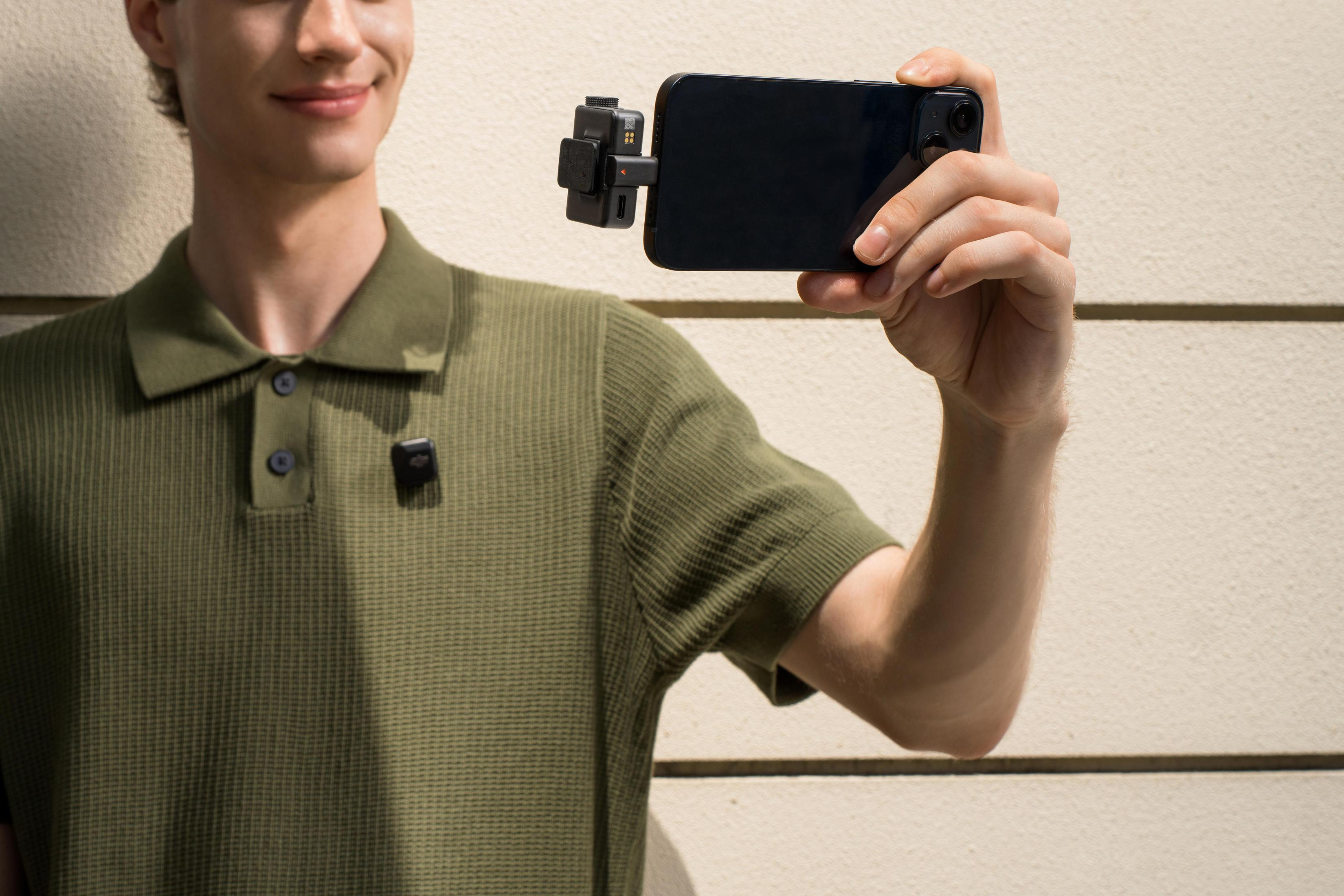 Mężczyzna trzymający smartfon z małym mikrofonem, uśmiechnięty. Beżowe tło.