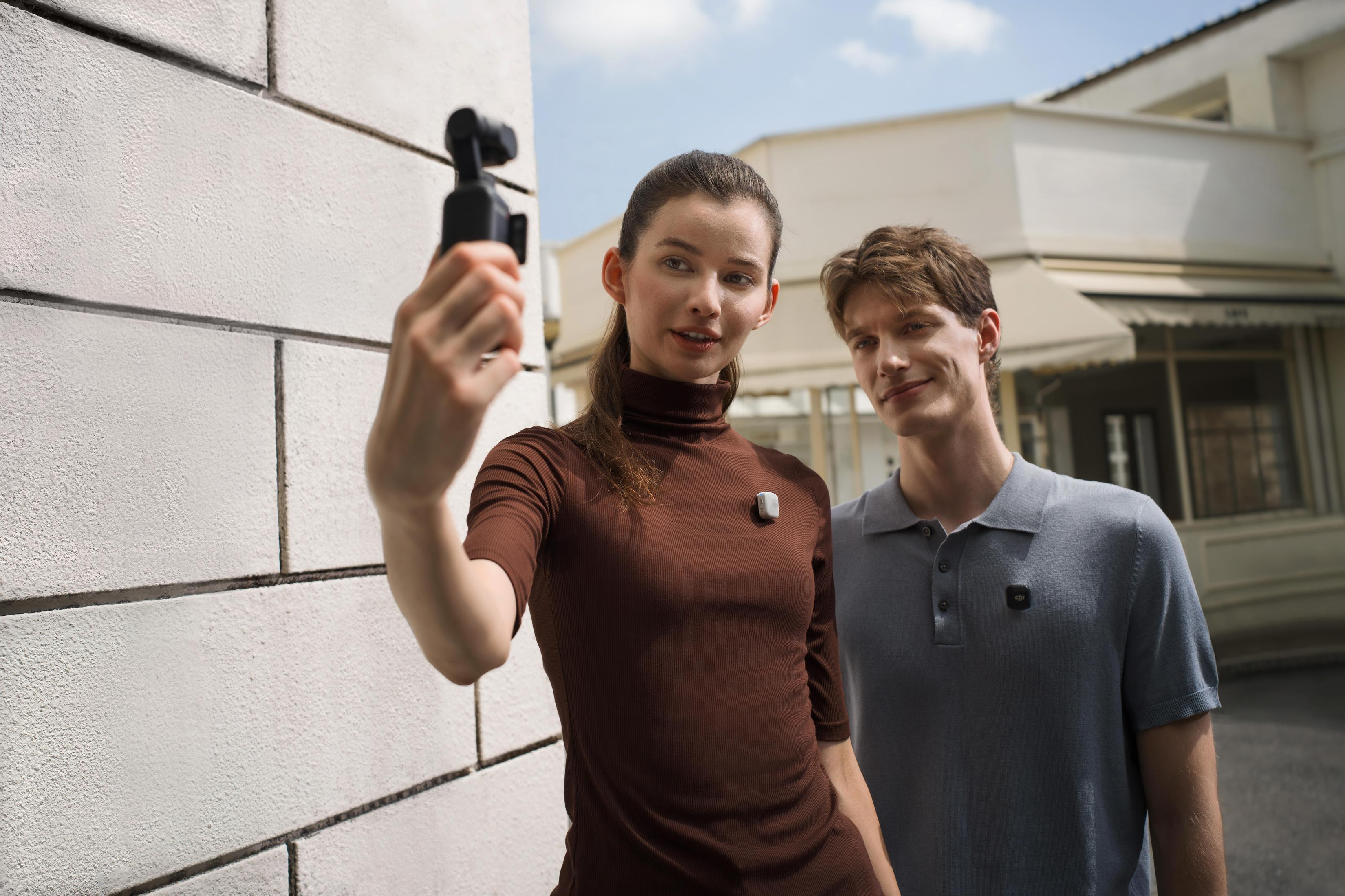 Dwie osoby robiące sobie selfie aparatem. Stoją obok białej ściany.