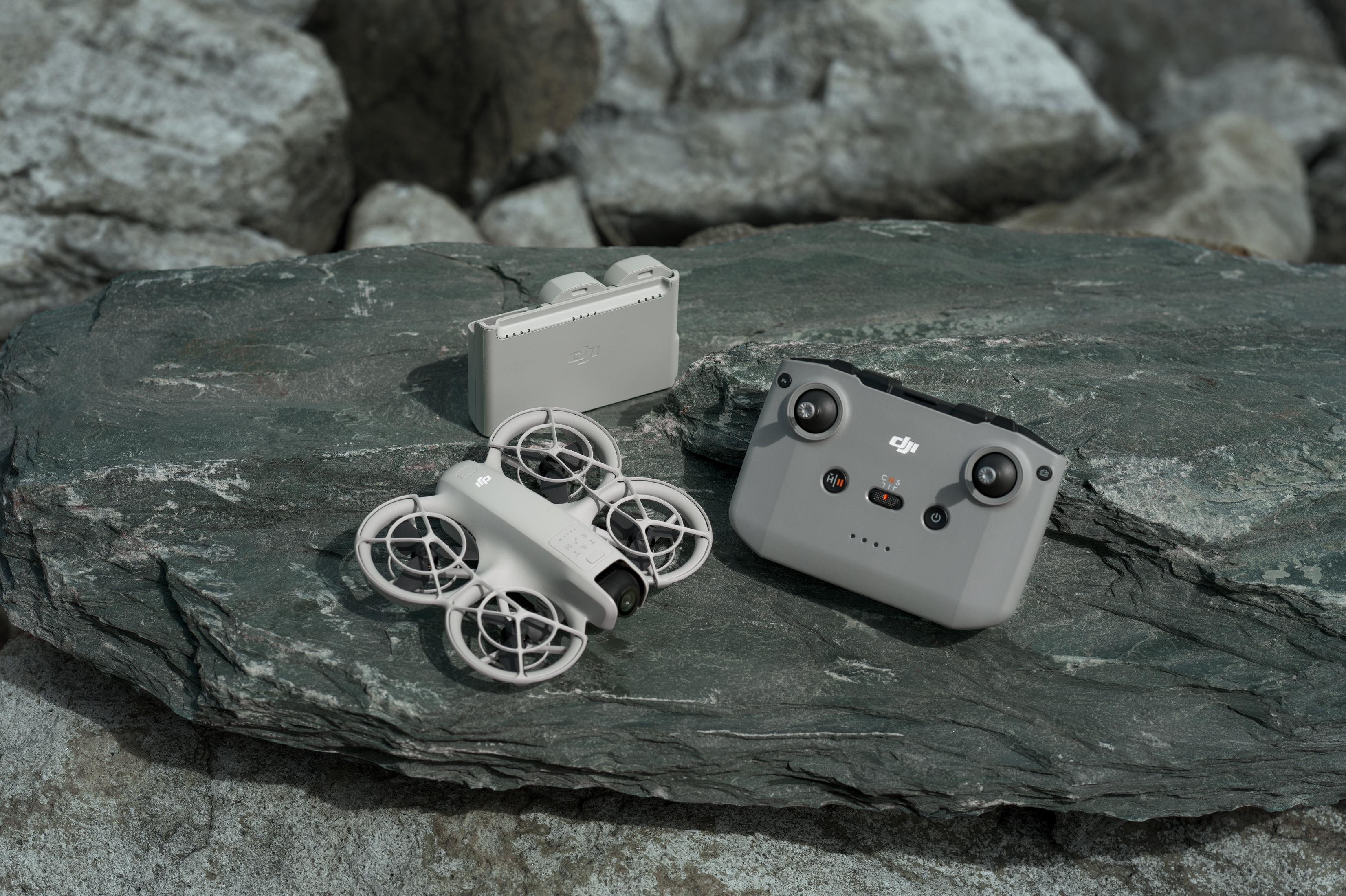 Eine Drohne, ein Controller und ein Ladekoffer liegen auf einer grauen Steinoberfläche. Die Drohne ist weiß.
