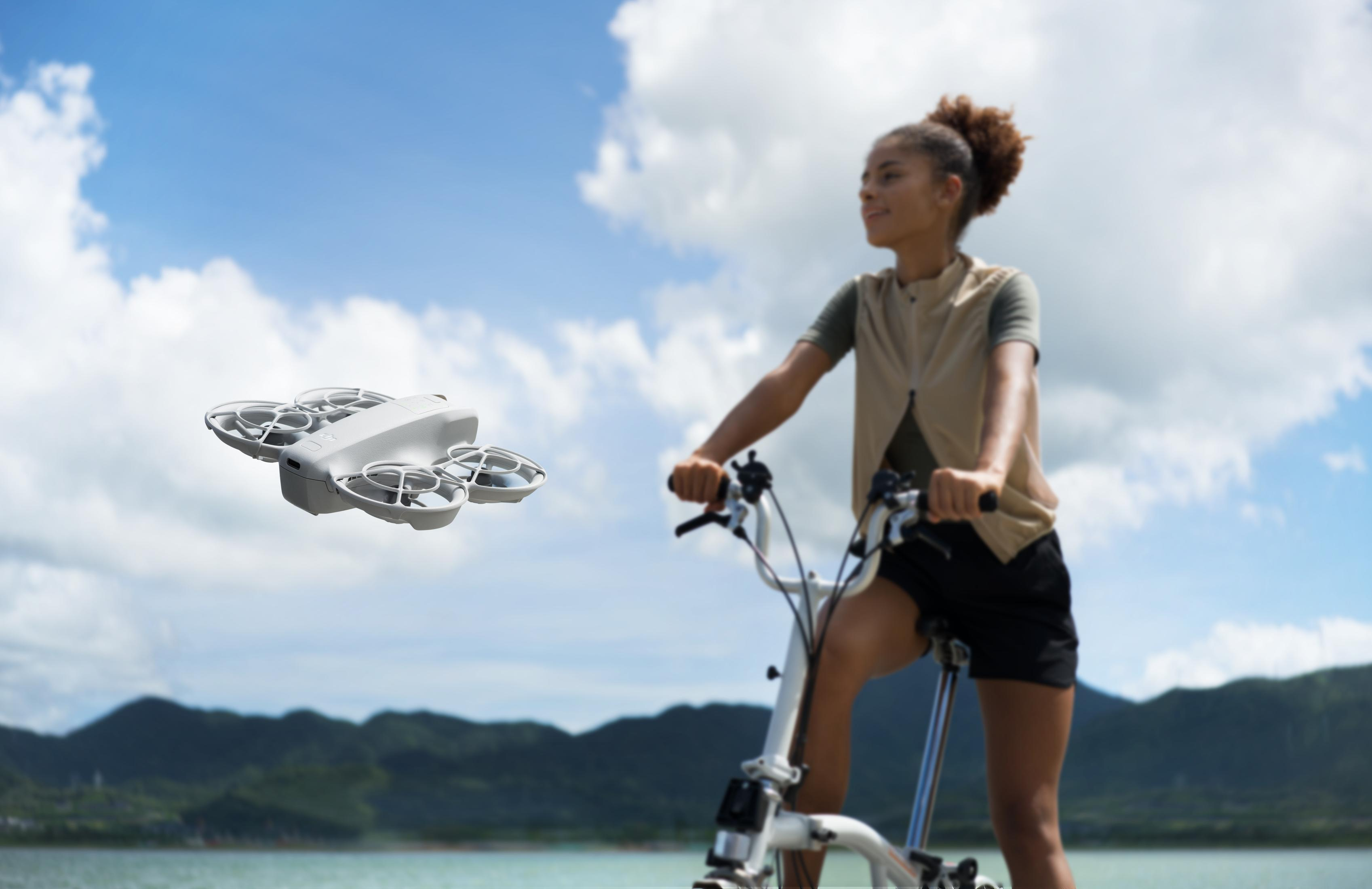 Eine Frau fährt Fahrrad, während eine Drohne an einem sonnigen Tag in der Luft fliegt.