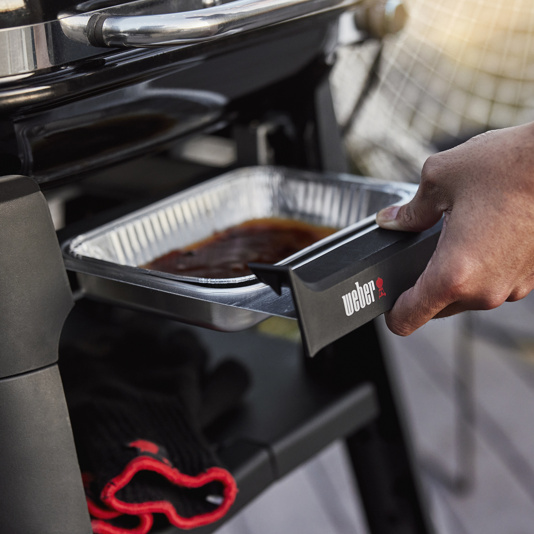 Persona che rimuove un vassoio con cibo da una griglia Weber, con griglia e guanti.