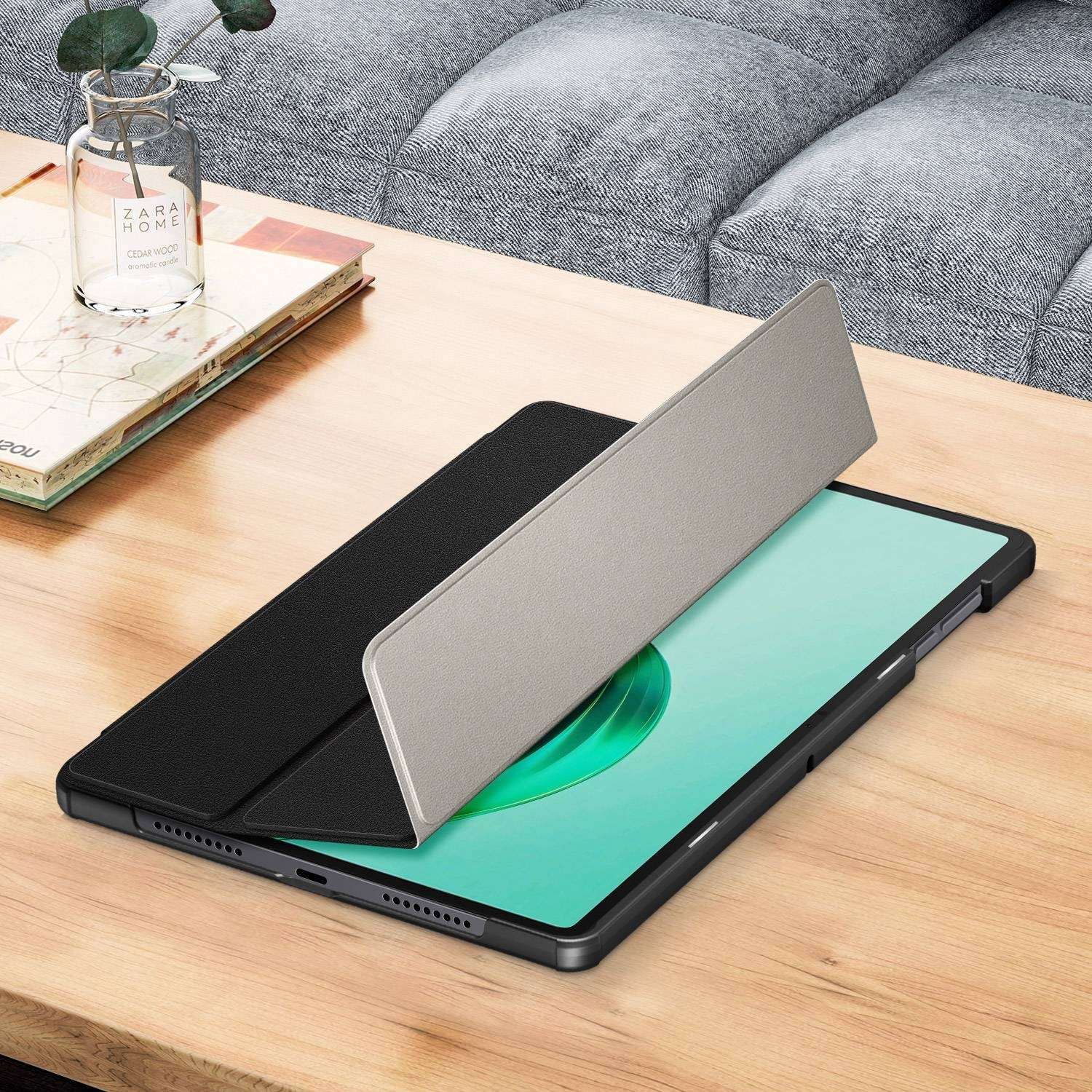 Tablet in einer schwarzen Hülle mit hellgrauer, offener Abdeckung. Auf einem Holztisch platziert.