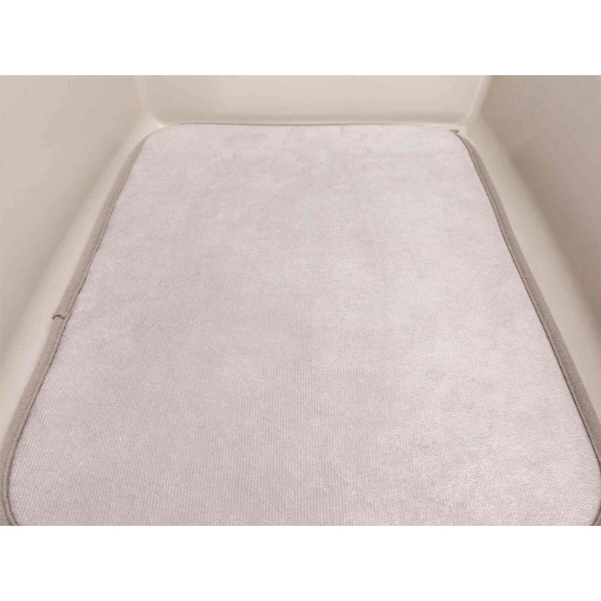 Tappetino da bagno rettangolare grigio chiaro all'interno di una vasca bianca. Il tappetino ha una trama sottile e un bordo grigio.