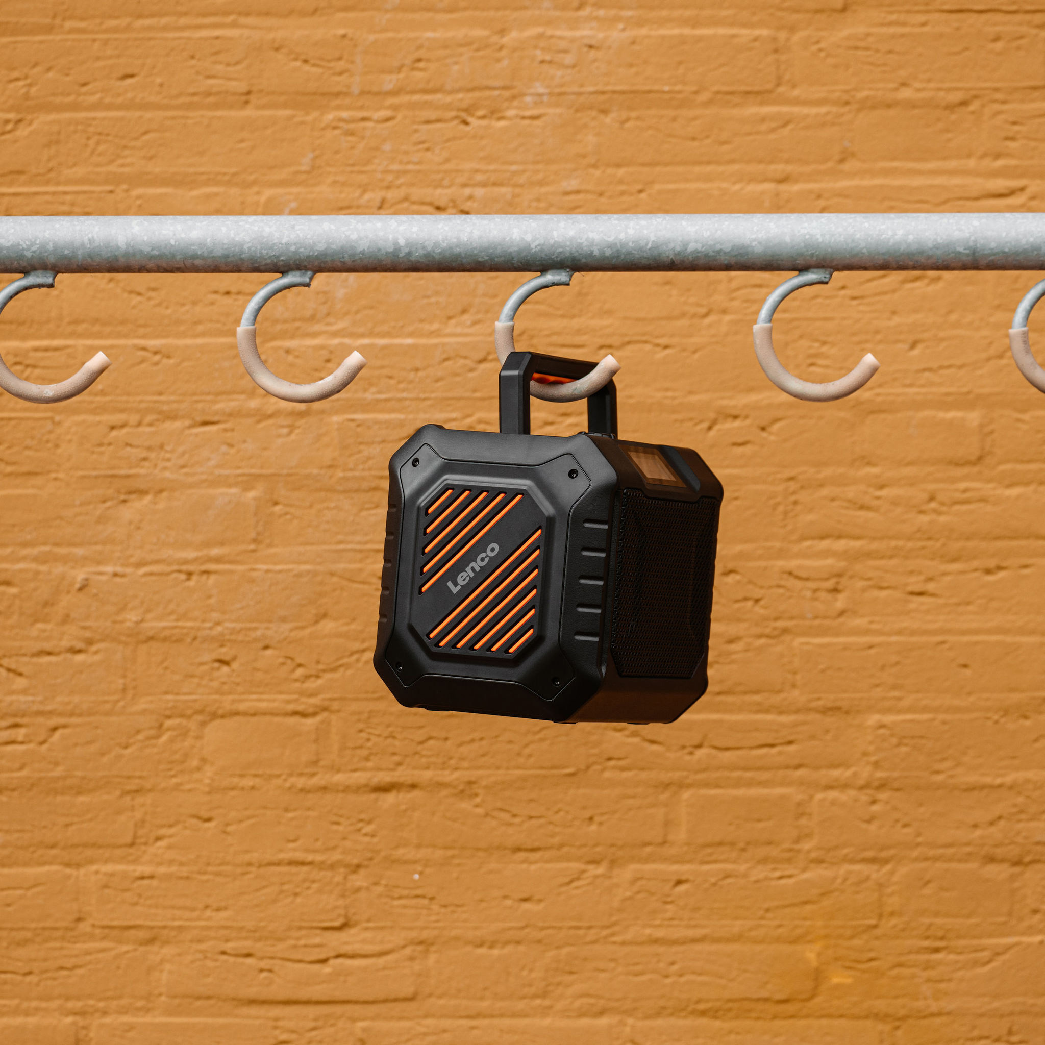 Czarny i pomarańczowy głośnik przenośny zawieszony na metalowym pręcie.