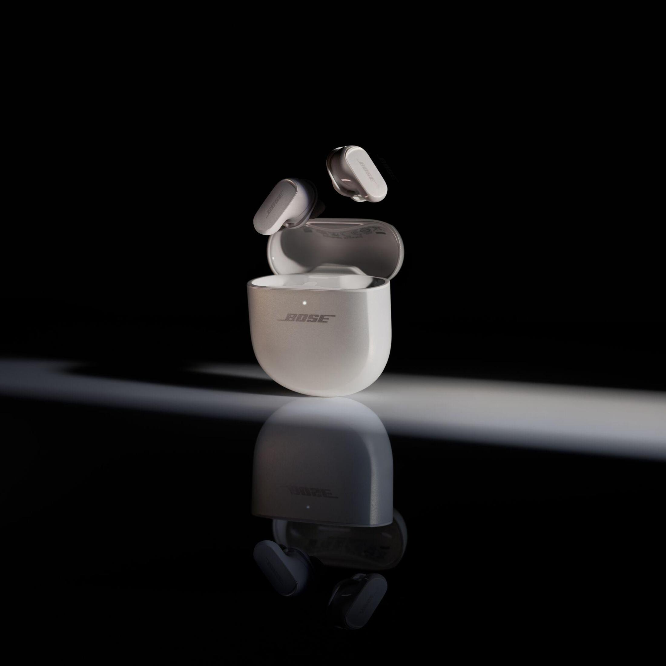 Białe słuchawki Bose i etui ładujące, unoszące się w powietrzu, z jasnymi i ciemnymi odbiciami.