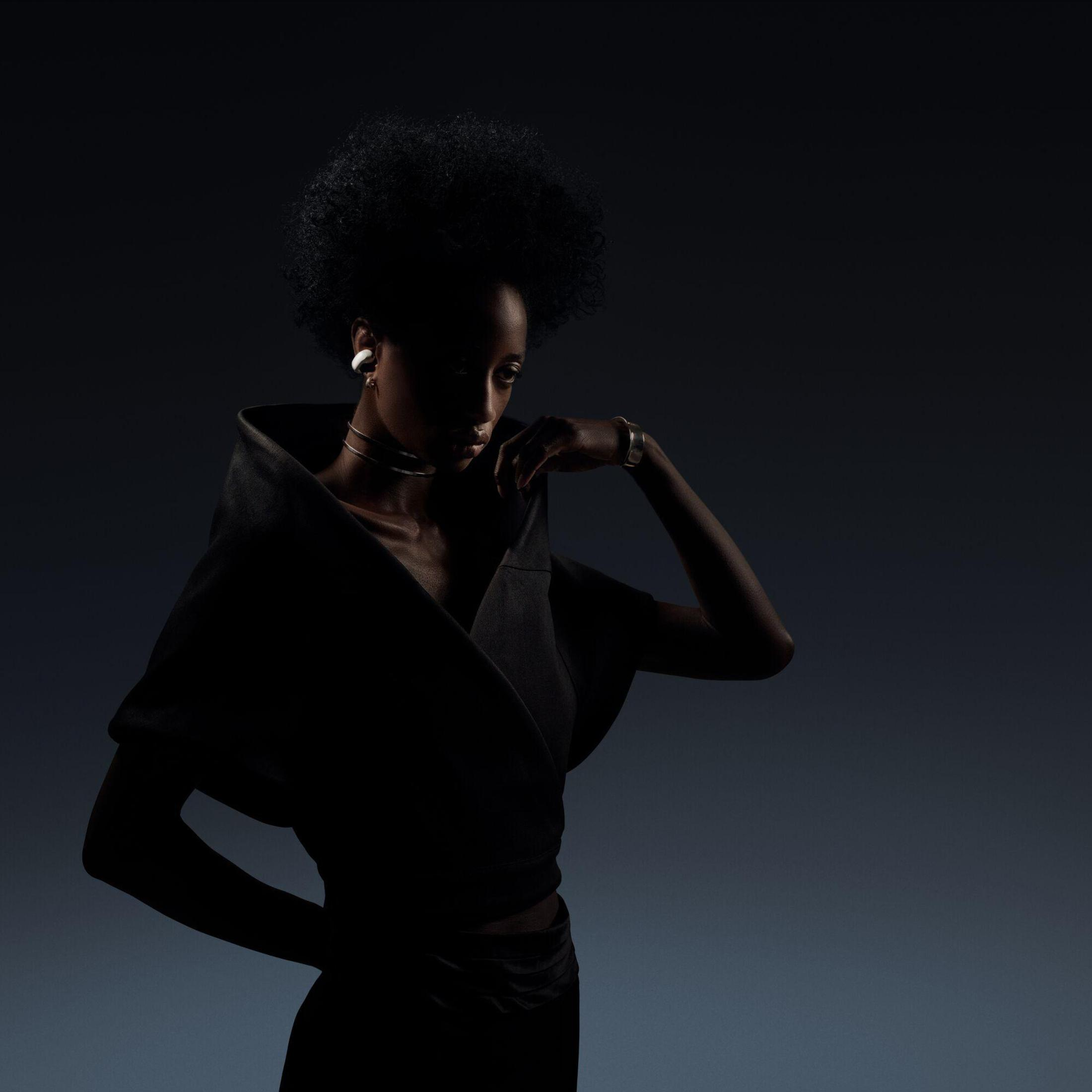 Sylwetka kobiety w czarnych ubraniach, skierowana w lewo, na tle ciemnoniebieskiego tła.