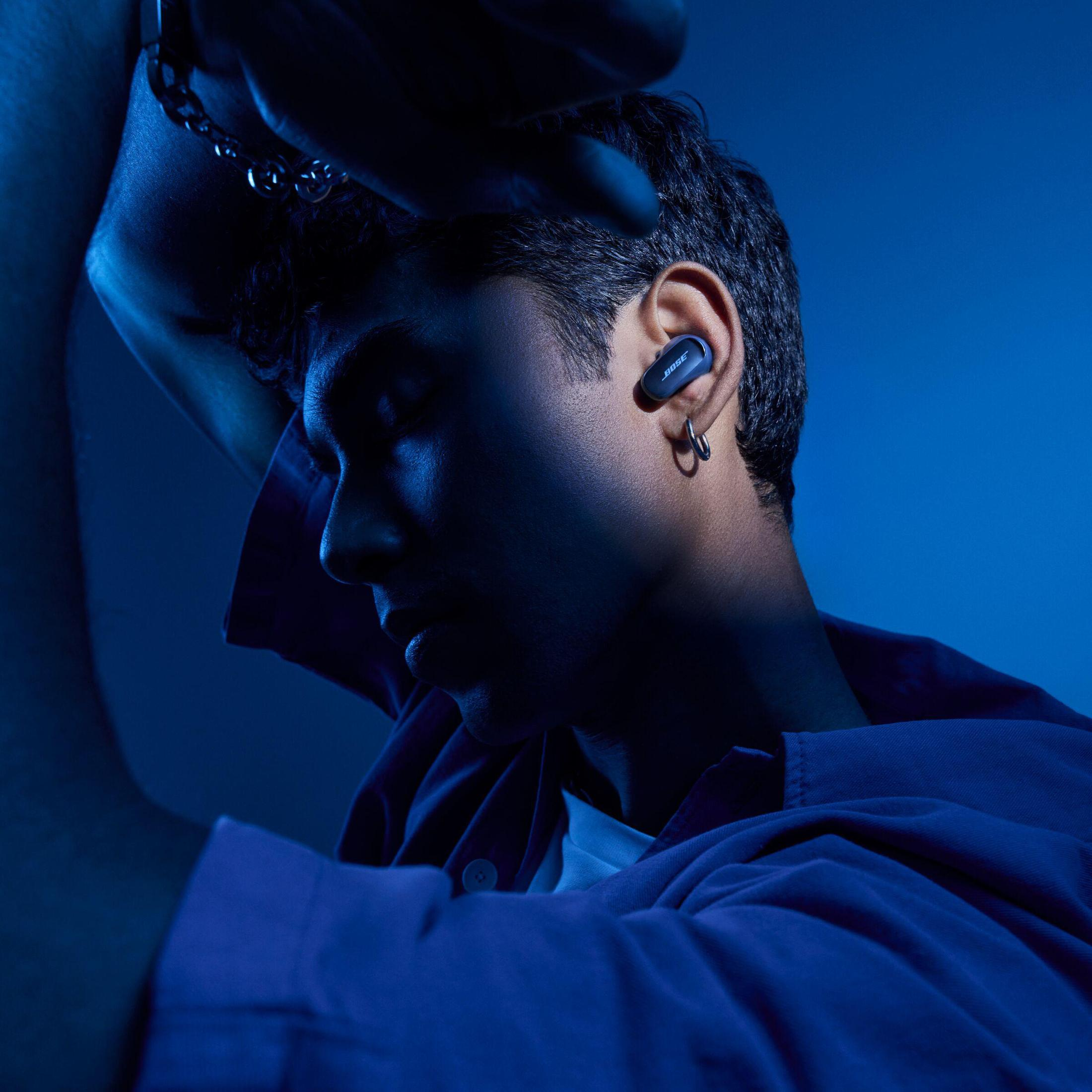 Osoba nosząca niebieską koszulę z niebieską słuchawką w uchu, zacieniona twarz.