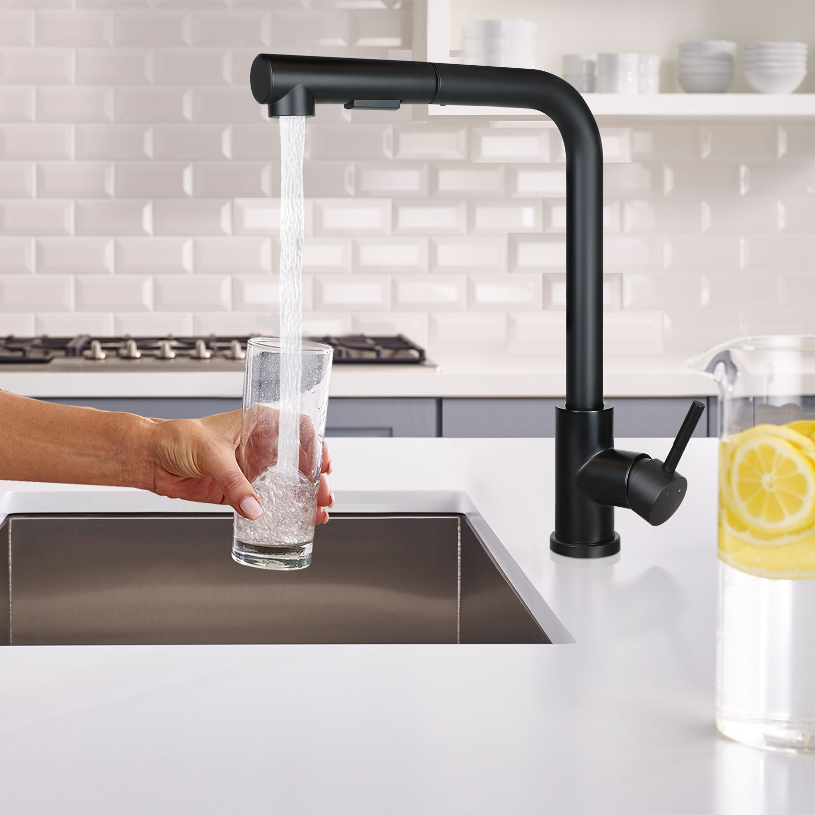 Ein schwarzer Wasserhahn, der Wasser in ein Glas gießt, das von einer Hand auf einer weißen Theke gehalten wird.