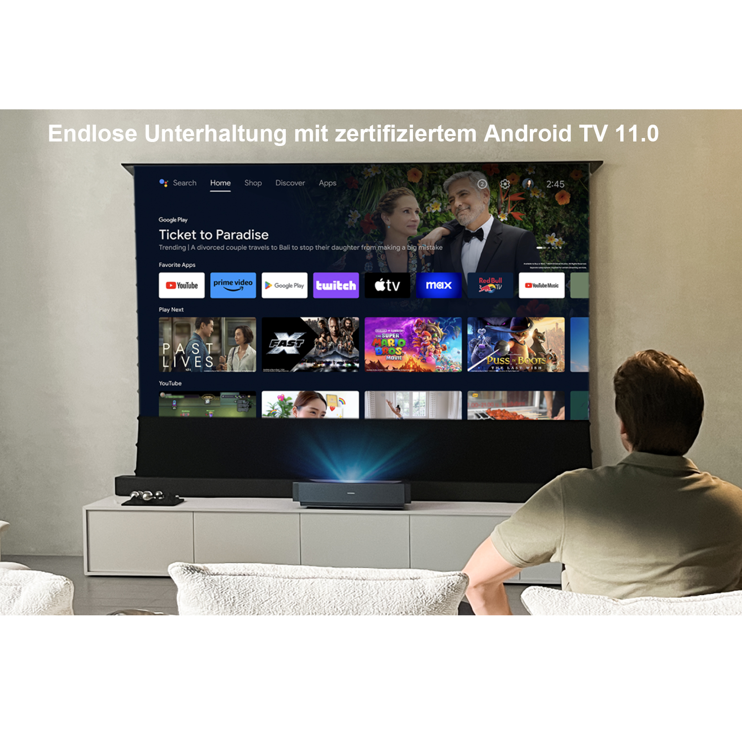 Ein Mann sieht sich einen großen Bildschirm an, der eine Streaming-Dienstoberfläche anzeigt. Der Raum hat weiße Wände und Möbel.