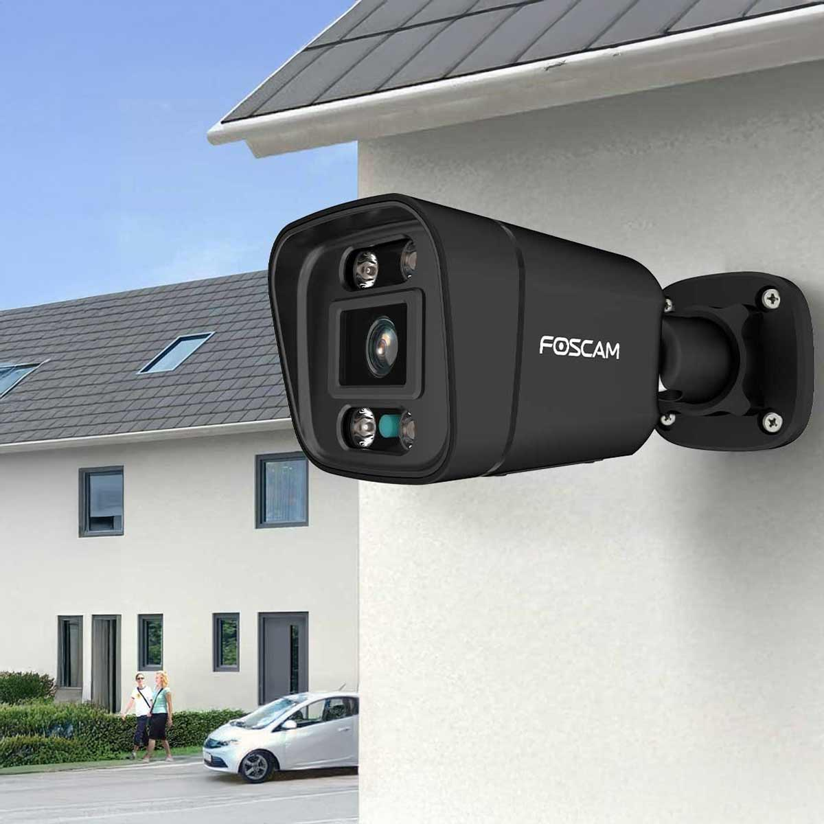 Czarna kamera bezpieczeństwa Foscam zamontowana na ścianie, z budynkiem w tle.