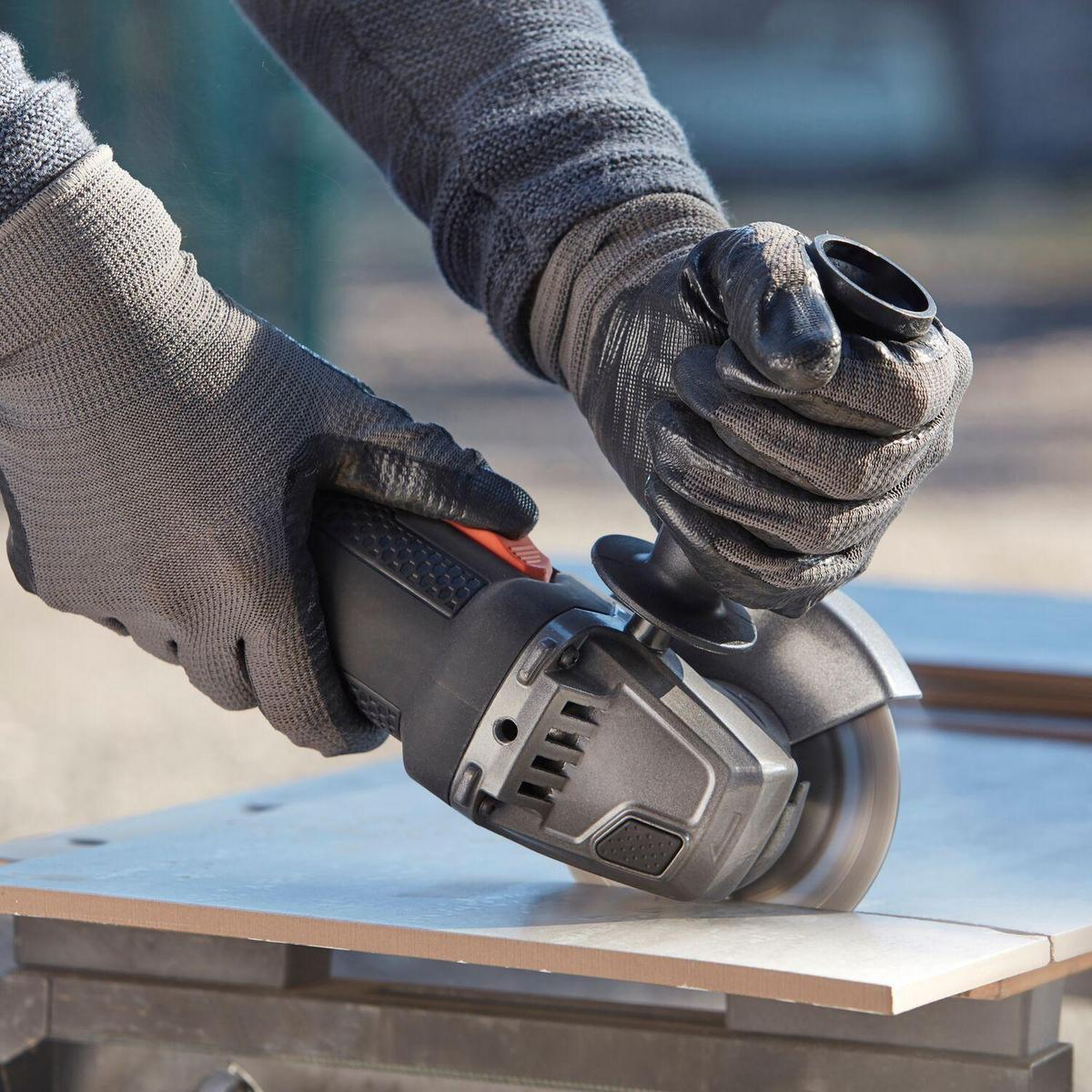 Manos con guantes usando una amoladora angular para cortar una baldosa. Baldosa sobre una mesa. Exterior.