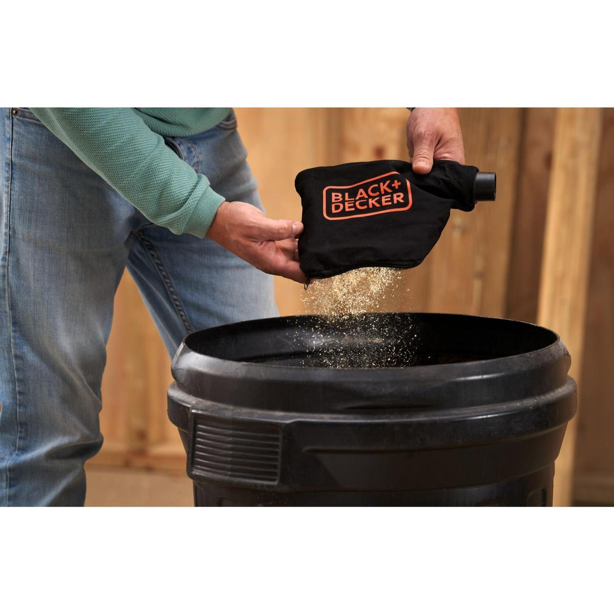 Una persona vaciando aserrín de una bolsa de polvo BLACK+DECKER en un cubo negro.