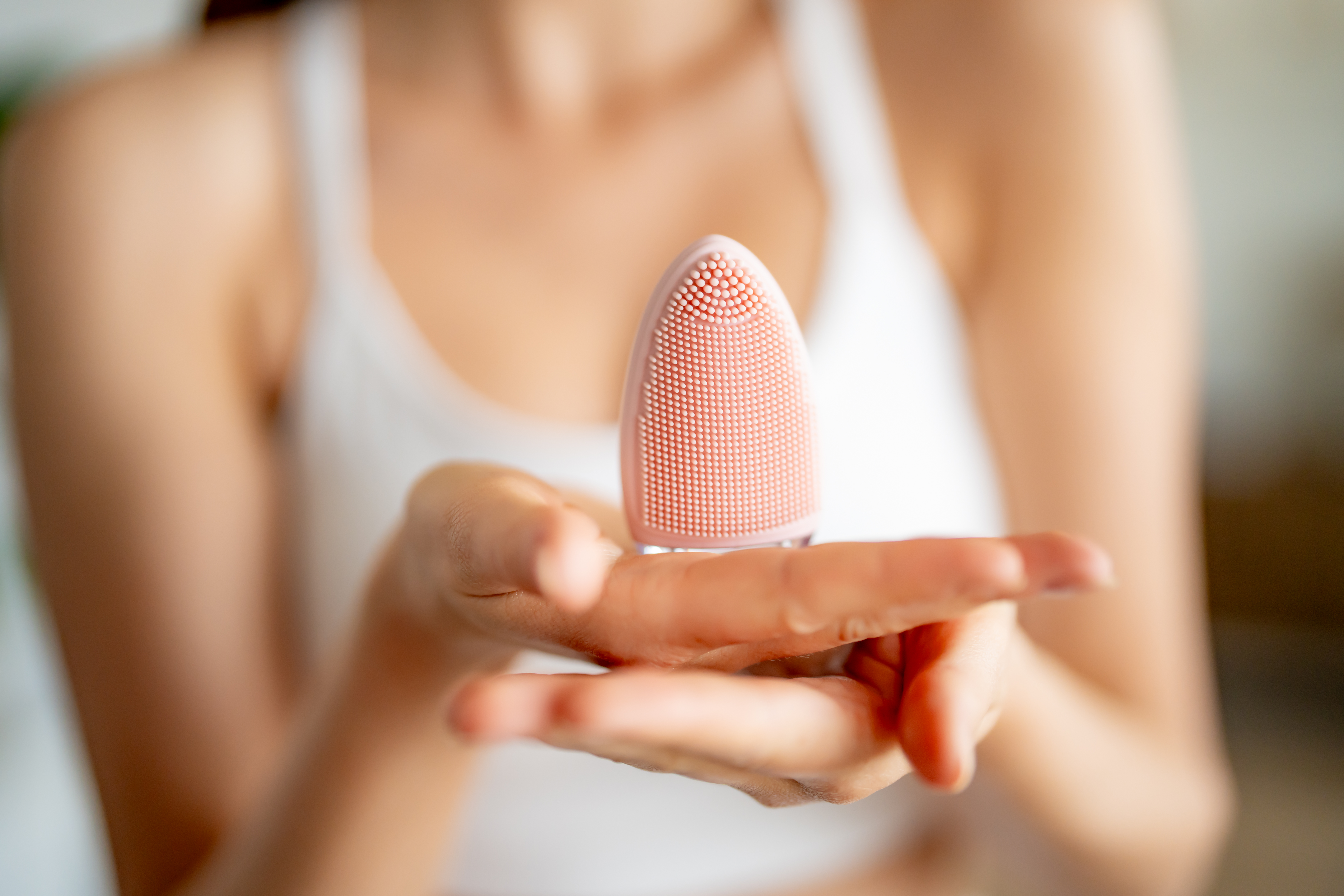 Persona sosteniendo un cepillo de limpieza facial rosa. El fondo está borroso.