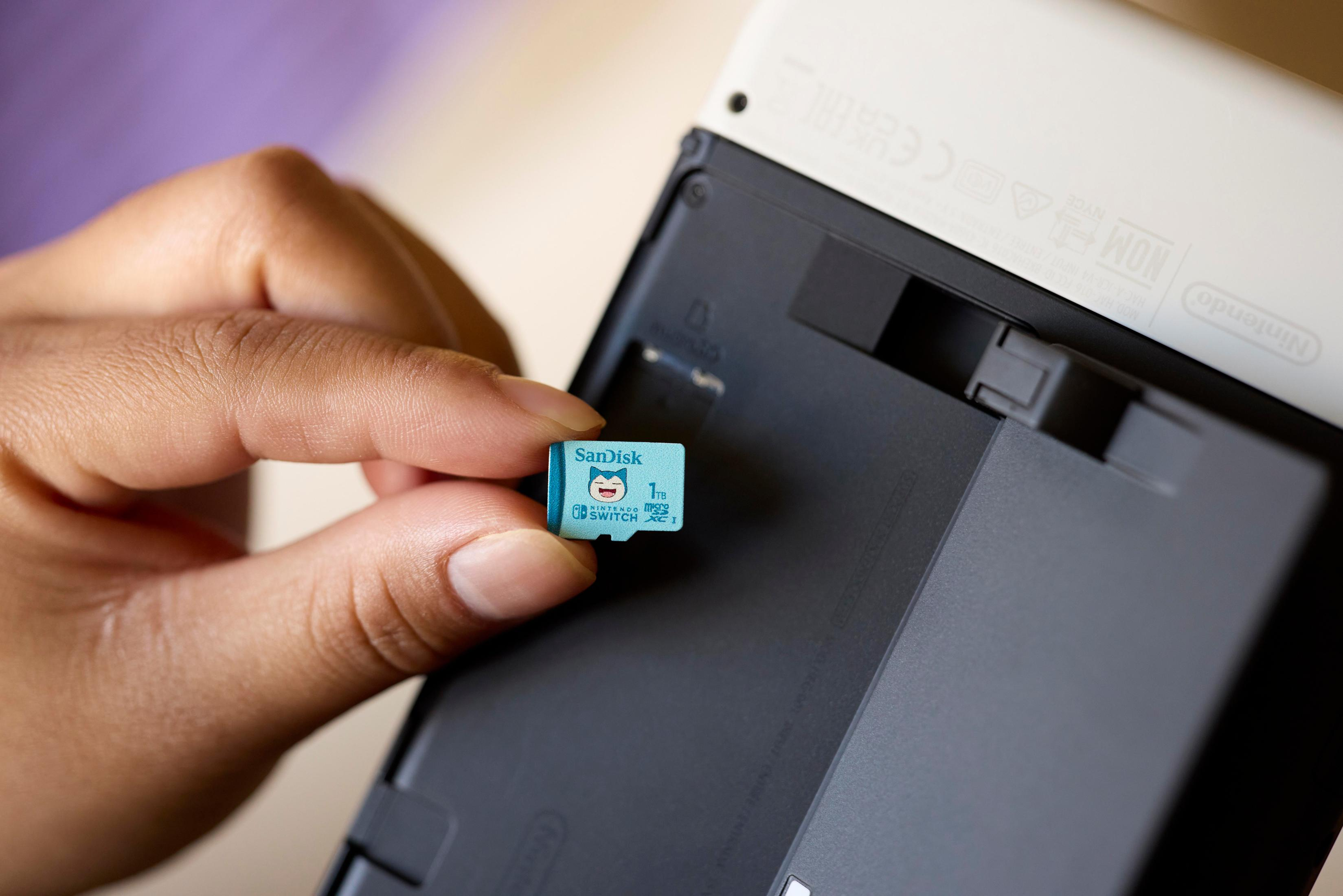 Hand hält eine Sandisk Micro-SD-Karte mit einer Nintendo Switch im Hintergrund.