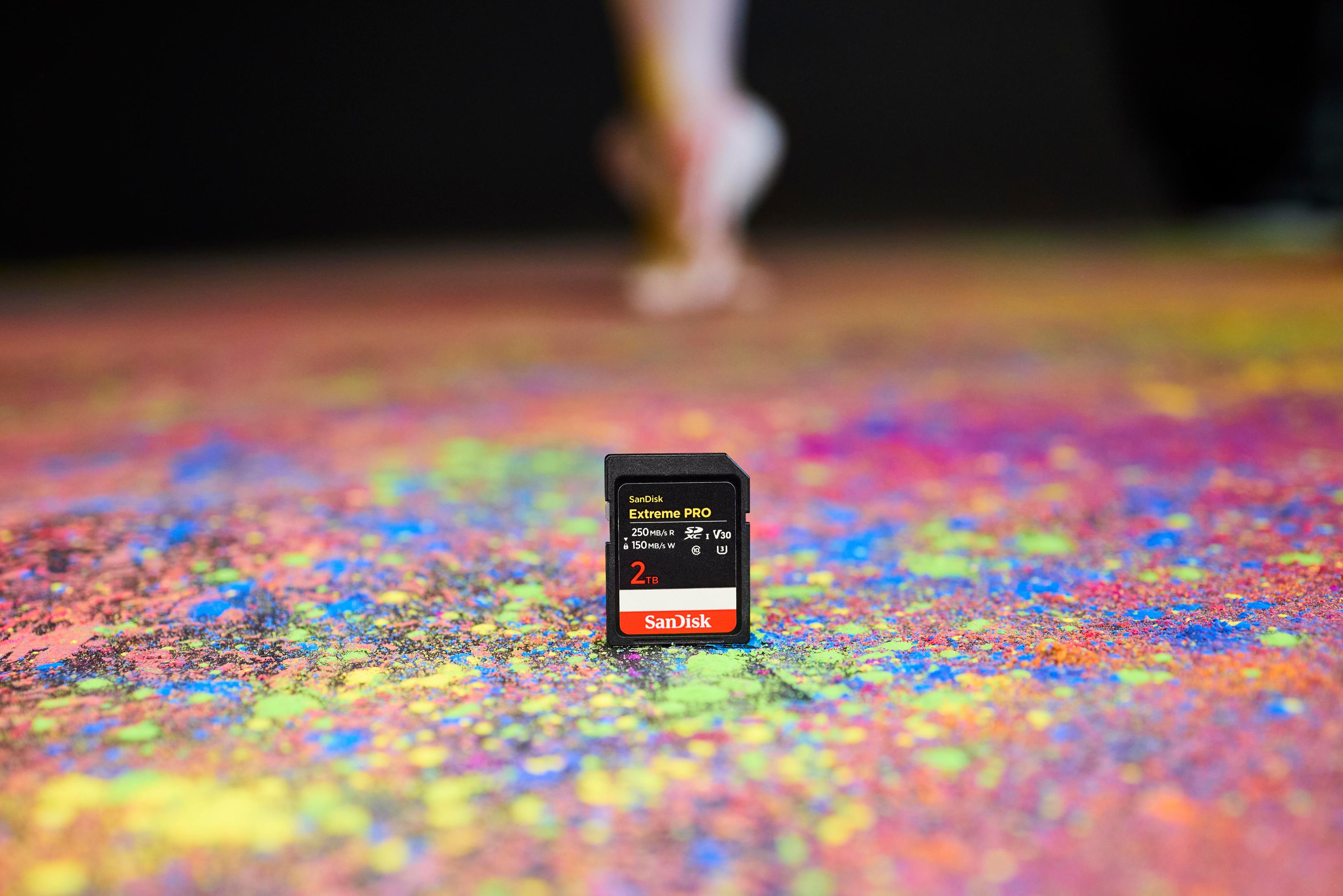 Sandisk Extreme PRO SD-Karte auf einer bunten, farbspritzerbedeckten Oberfläche mit unscharfem Hintergrund.
