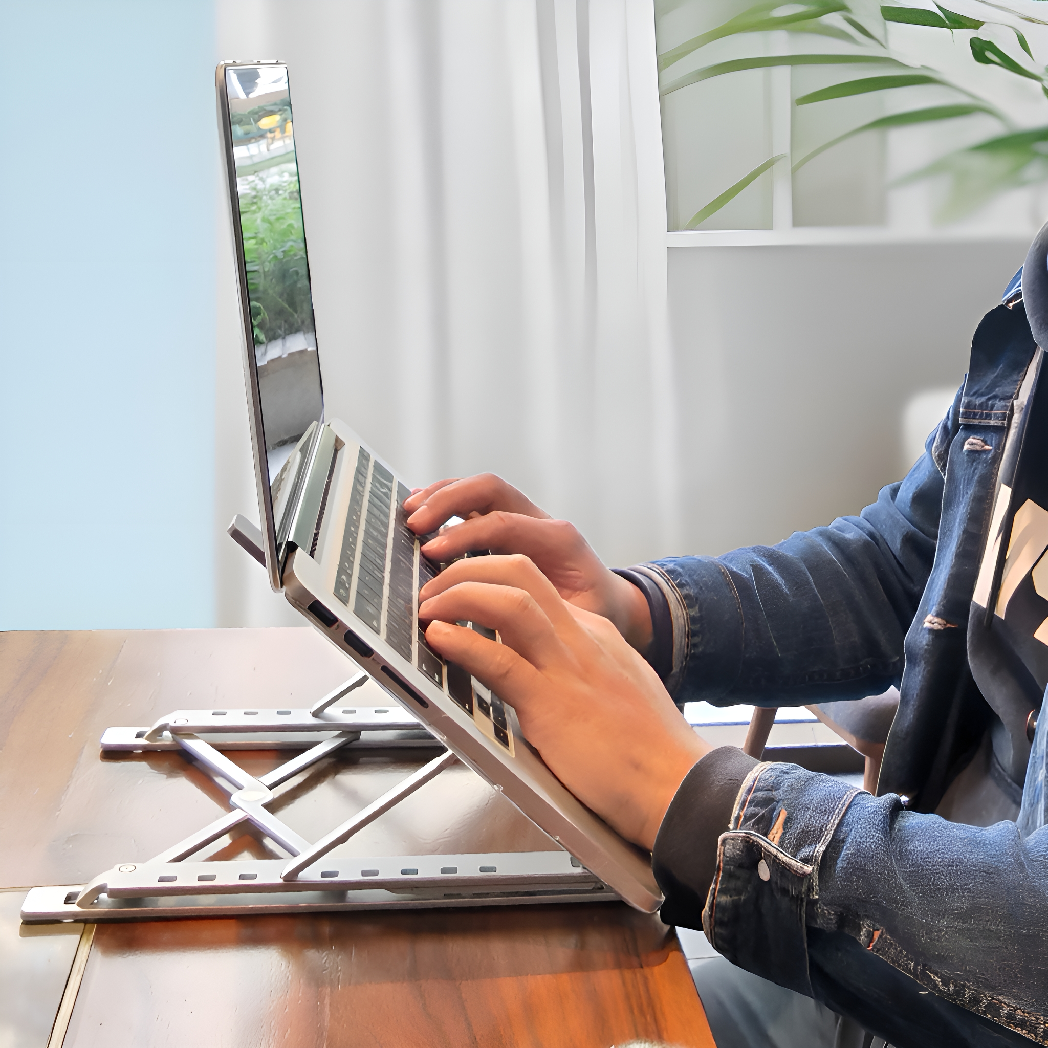 Person benutzt Laptop auf silbernem Ständer. Der Laptop-Bildschirm ist nach oben geneigt.