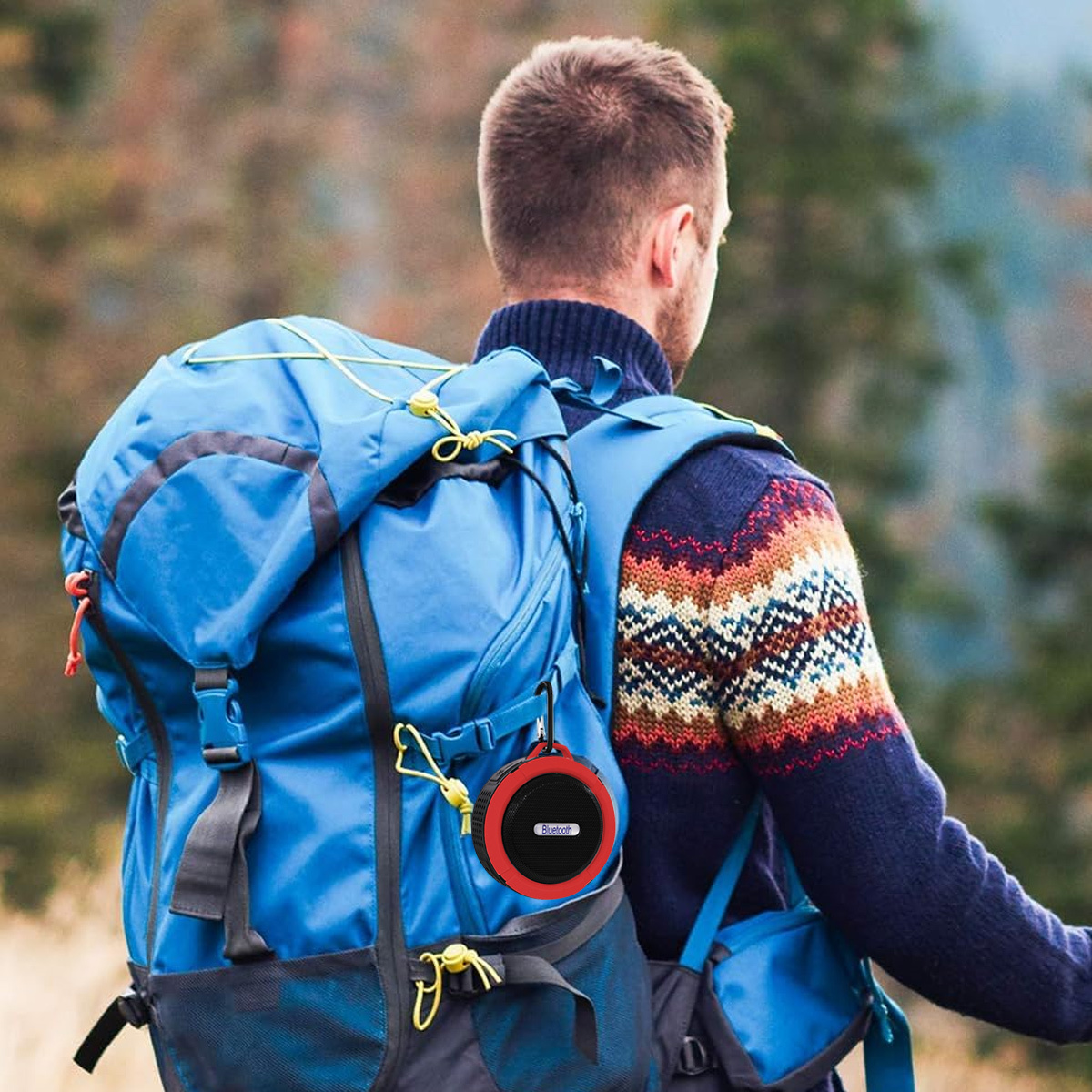 Mann mit Rucksack, trägt einen Pullover, trägt einen roten Bluetooth-Lautsprecher am Rucksack.