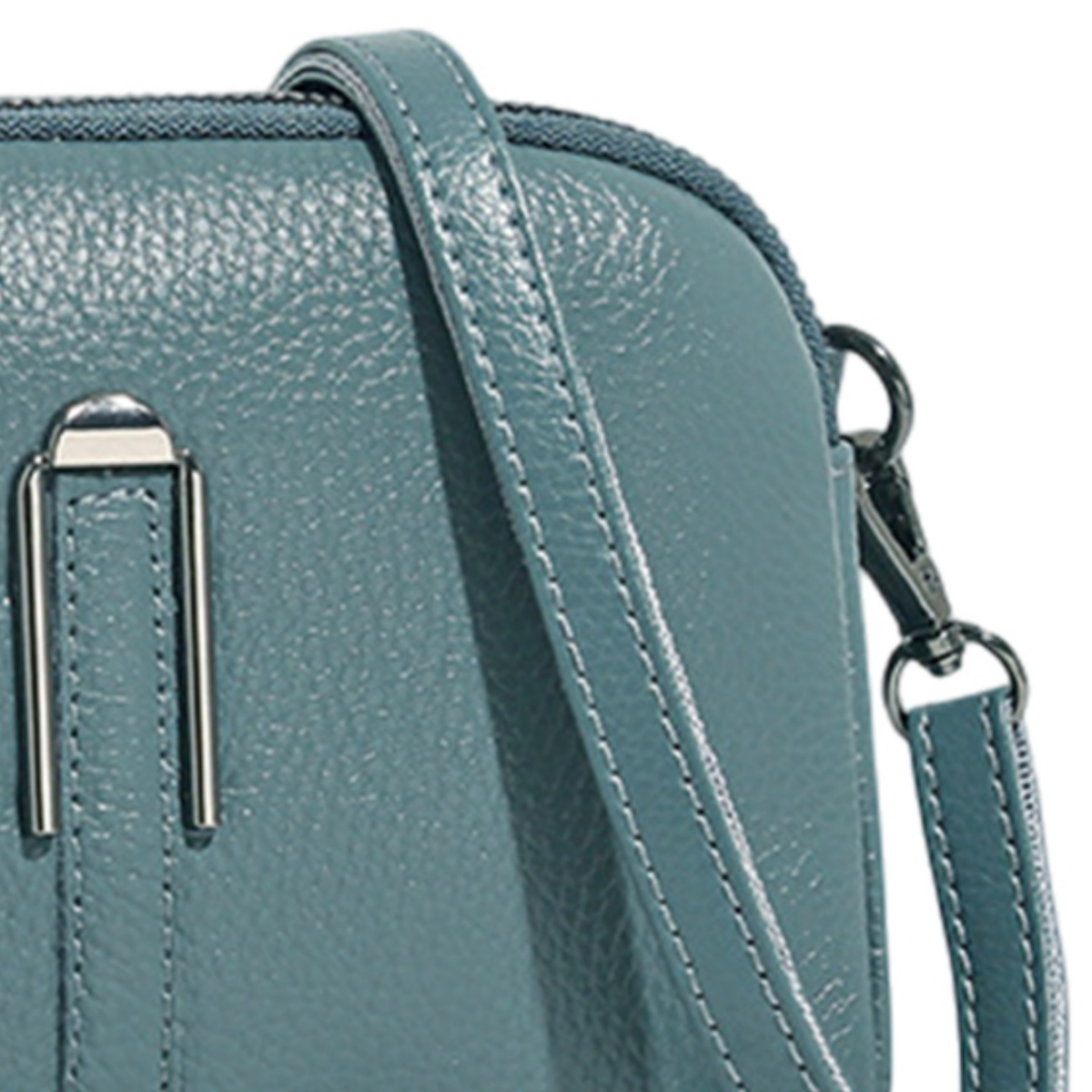 Nahaufnahme einer teal-farbenen Ledertasche mit Riemen und silbernen Beschlägen.