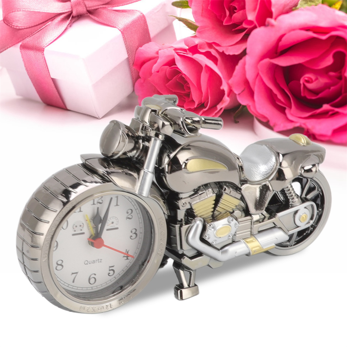 Chrom-Motorraduhr auf weißer Oberfläche mit rosa Blumen und Geschenkbox.