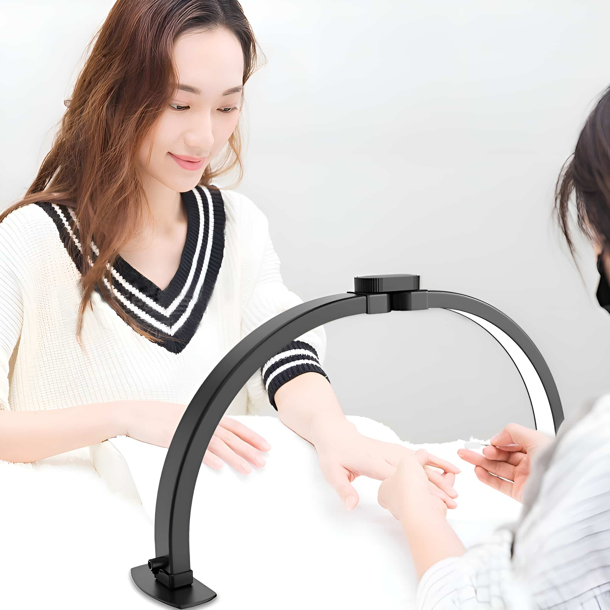 Eine Frau erhält eine Maniküre unter einer schwarzen, gebogenen LED-Lampe. Eine andere Person führt die Maniküre durch.