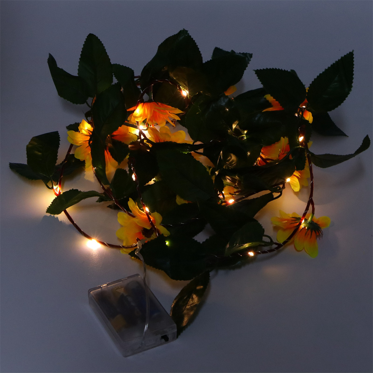 Lichterkette mit gelben Blumen und grünen Blättern auf weißem Untergrund.