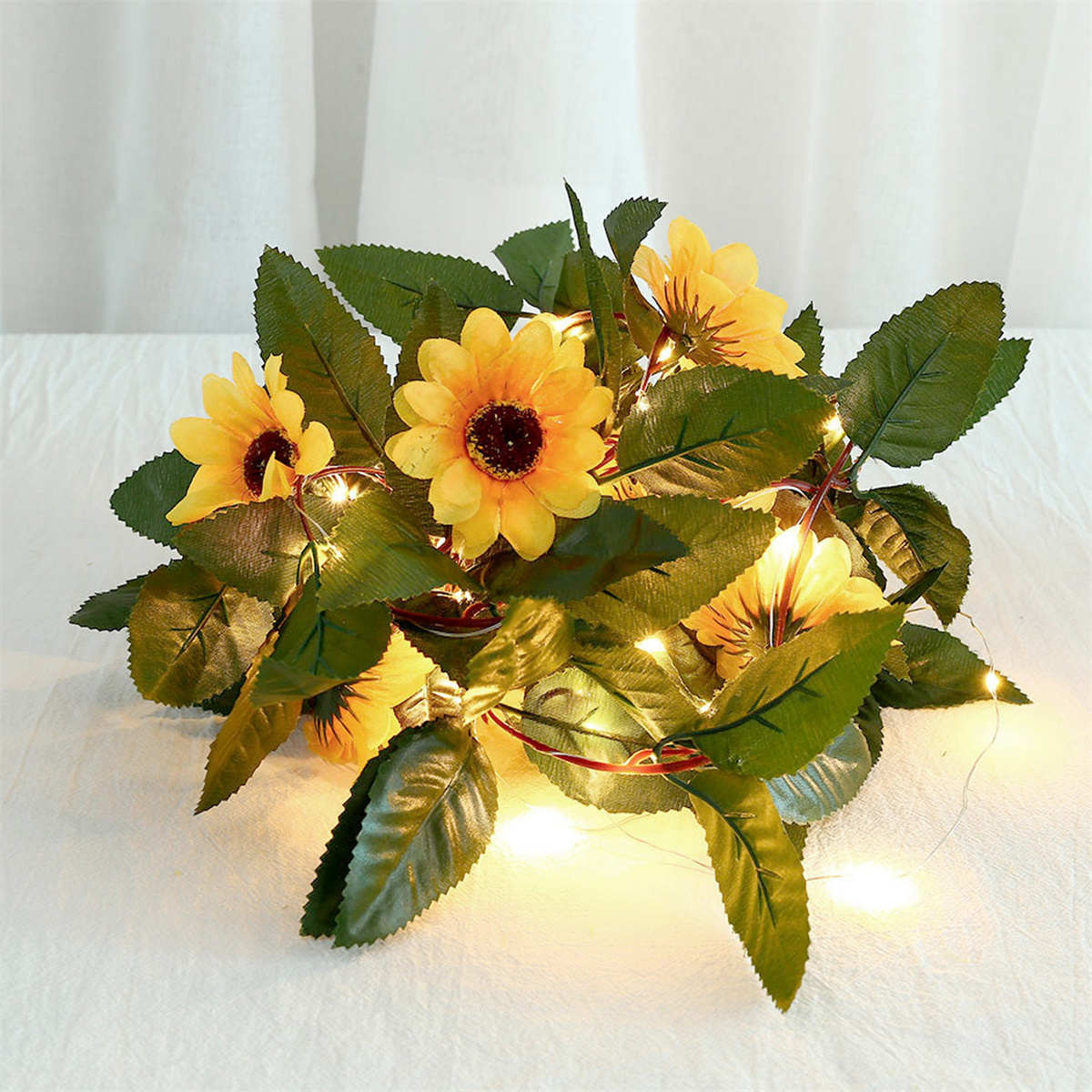 Sonnenblumenarrangement mit Lichtern auf weißer Oberfläche. Grüne Blätter und gelbe Blüten.