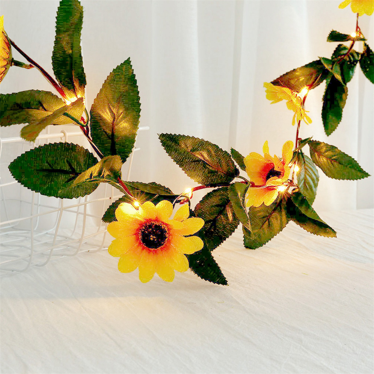 Eine Girlande aus künstlichen Sonnenblumen mit Lichtern. Die Girlande befindet sich auf weißem Hintergrund.