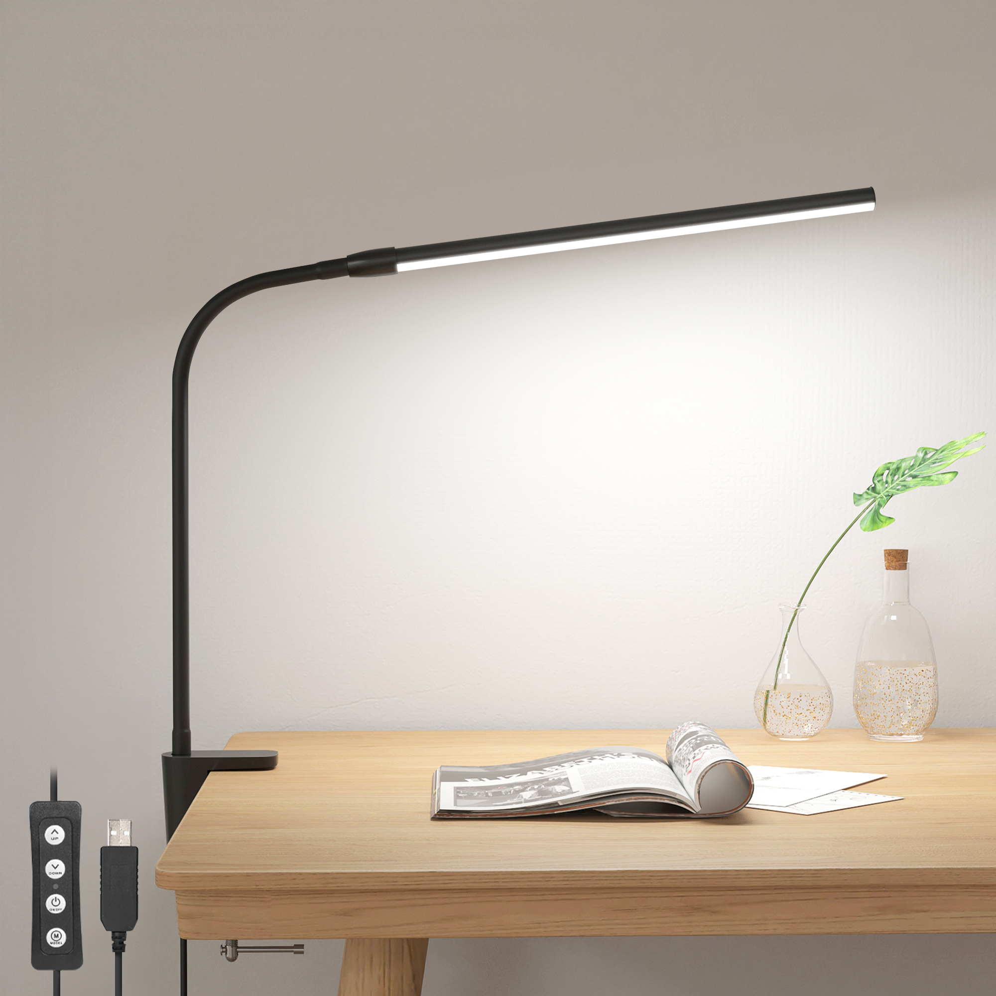 Eine schwarze Schreibtischlampe mit biegsamem Arm, die einen Schreibtisch mit Buch und Pflanze beleuchtet.
