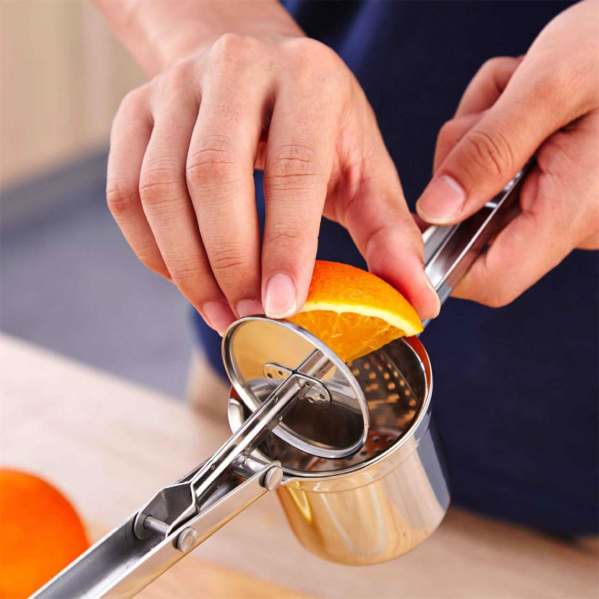 Eine Person presst eine Orangenhälfte mit einer manuellen Saftpresse, mit einer Orangenscheibe in der Presse.