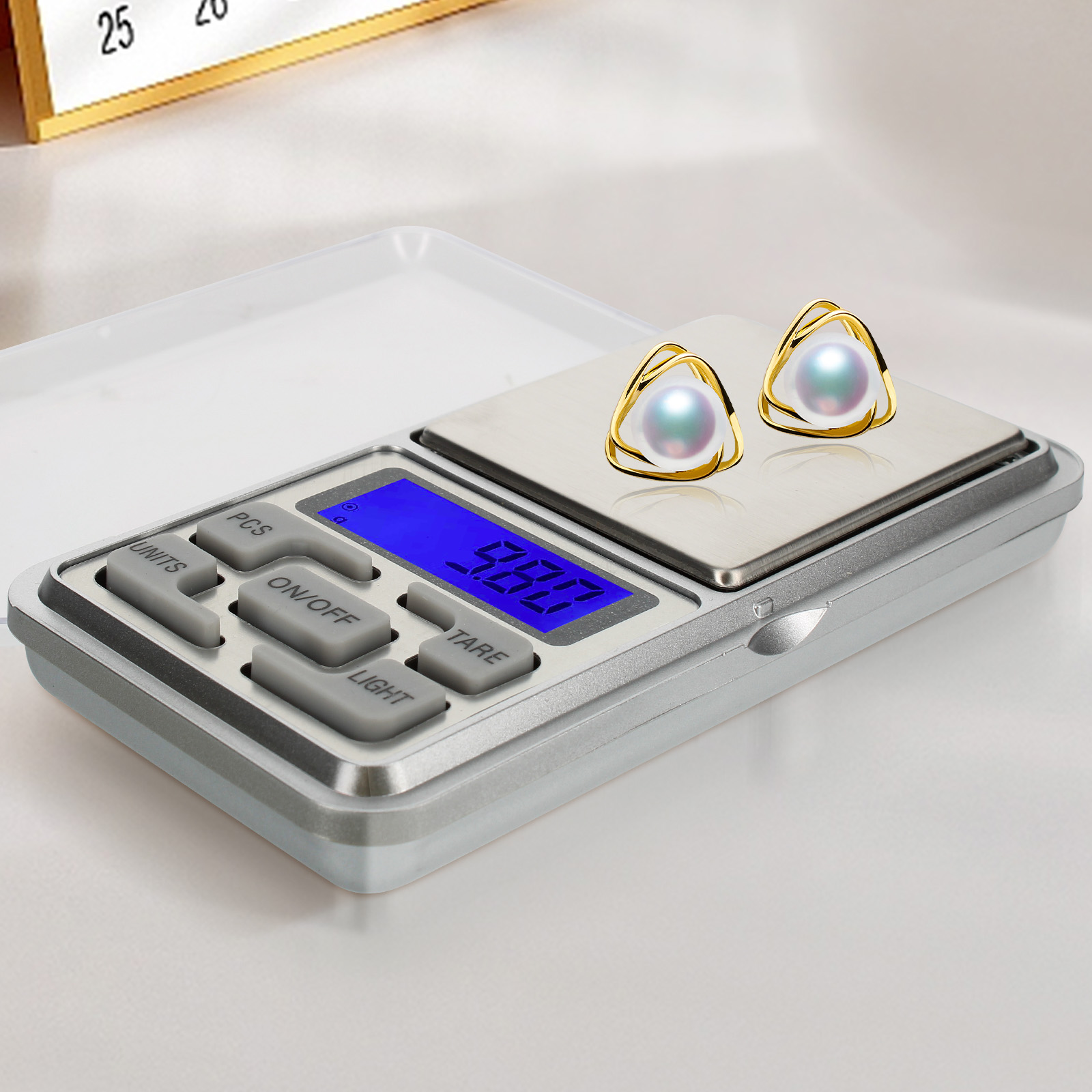 Digitale Waage mit zwei goldenen Ohrringen mit Perlen. Anzeige zeigt '5.80'.
